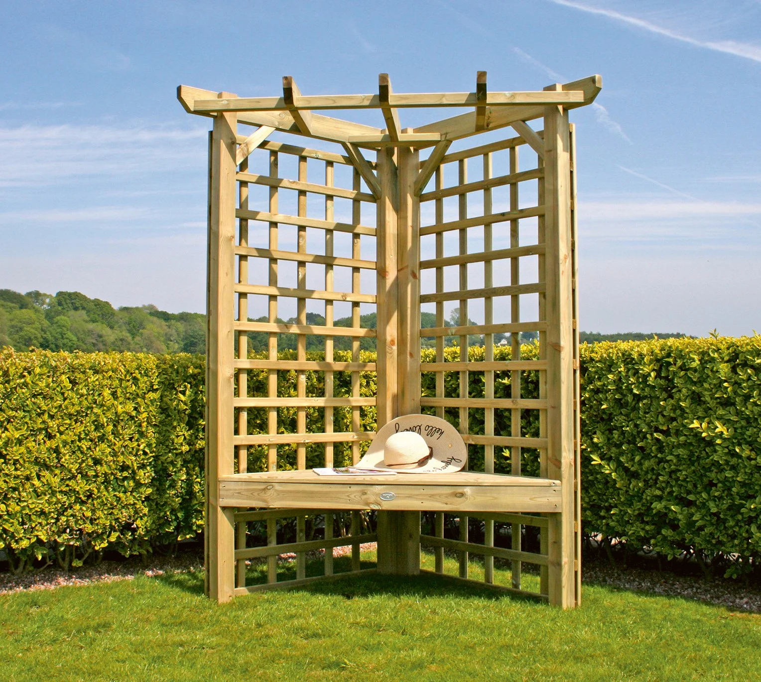 Wooden garden arbor with lattice panels, bench, and straw hat, surrounded by green hedges and grassy lawn.