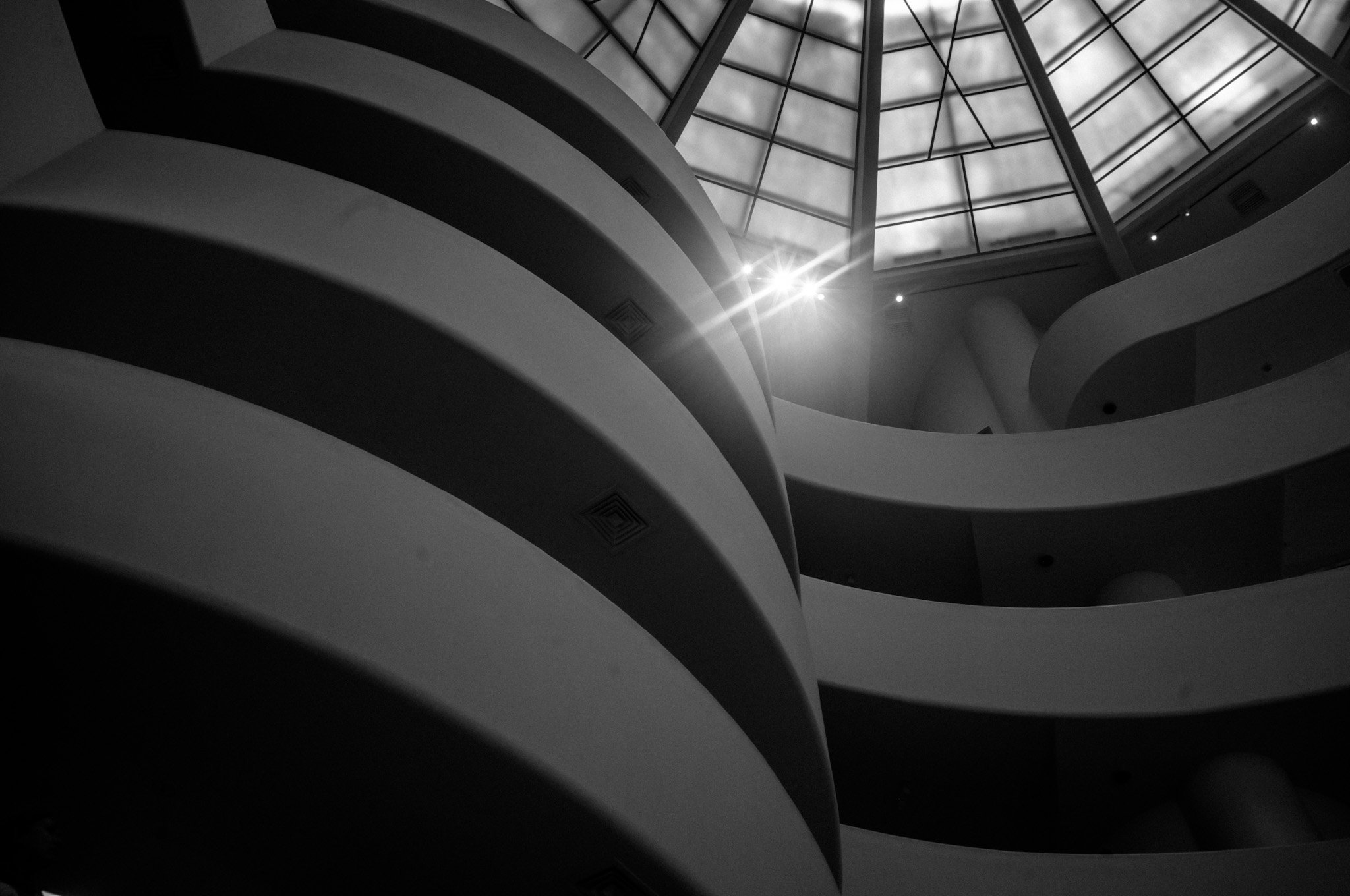 Black and white interior view of a modern building, showing curved balconies and a glass ceiling with natural light coming through.
