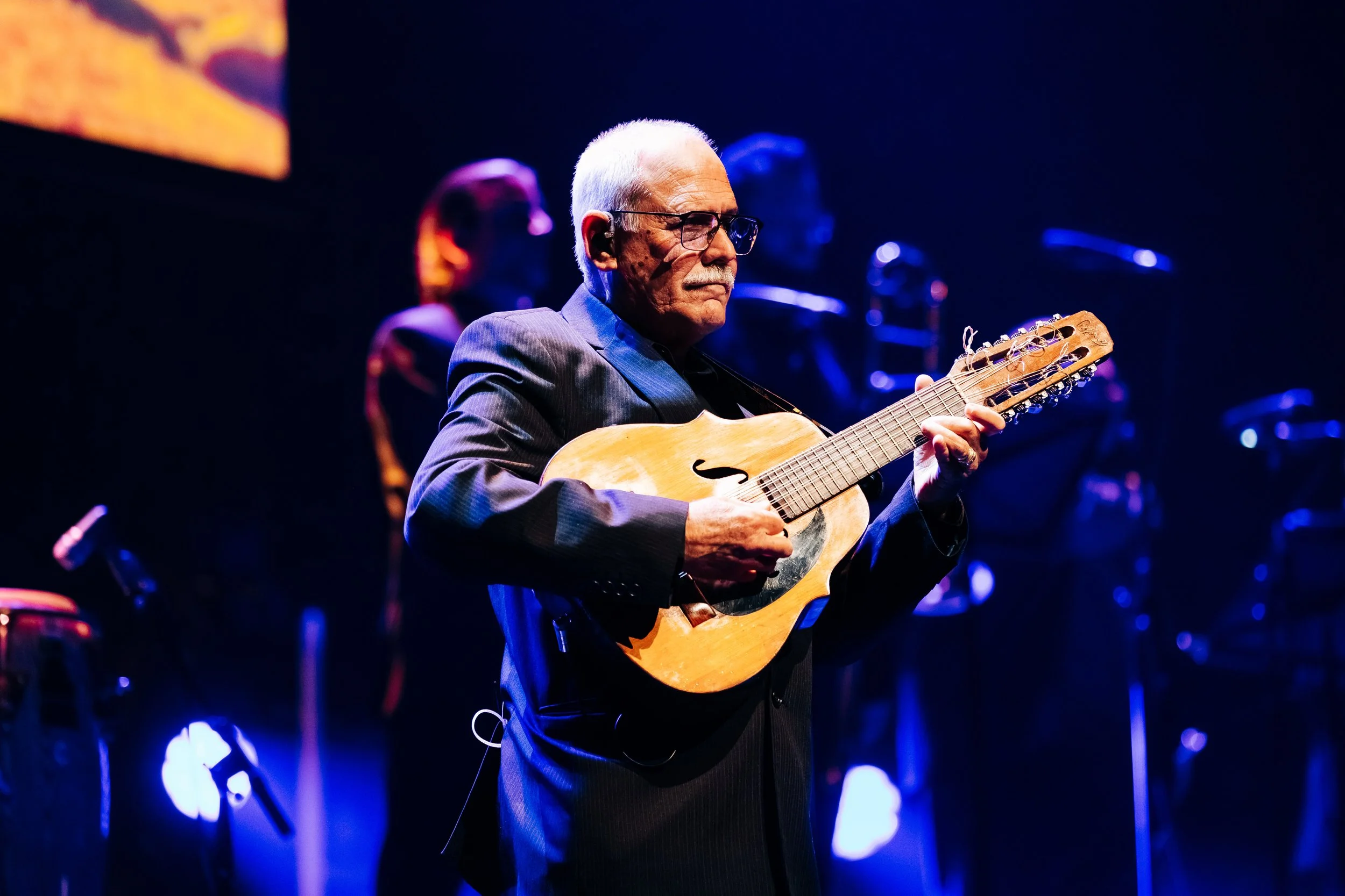 An elderly man wearing glasses and a dark suit playing a guitar on stage with blue and purple lighting. Live event and concert photography taken by Mark Gillies Photography based in Glasgow. Mark covers music events, charity balls and concerts.