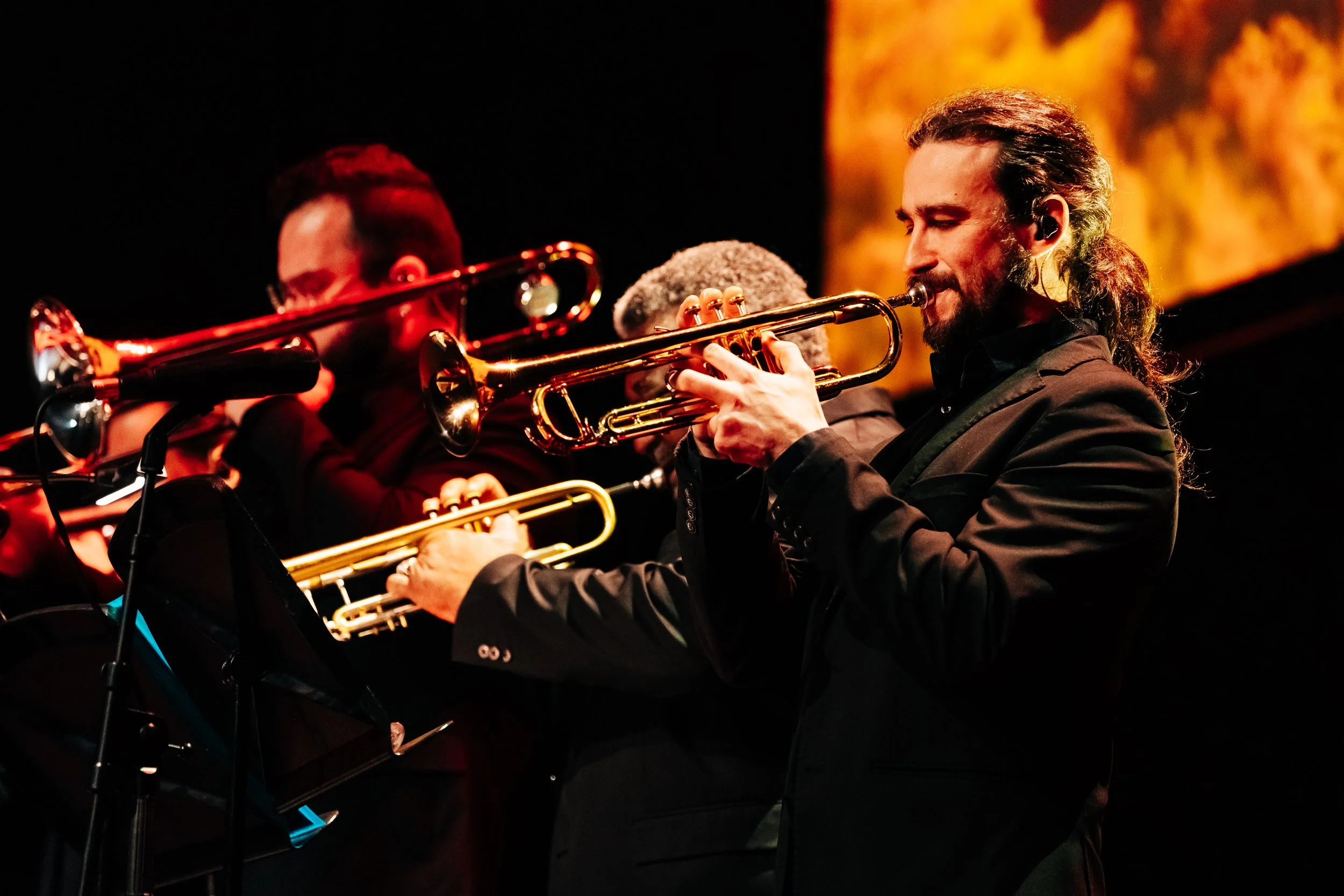 Three jazz musicians playing trumpets on stage, with a warm orange background. Live event concert photography at Royal Concert Hall in Glasgow by Mark Gillies for Buena Vida All Stars. 