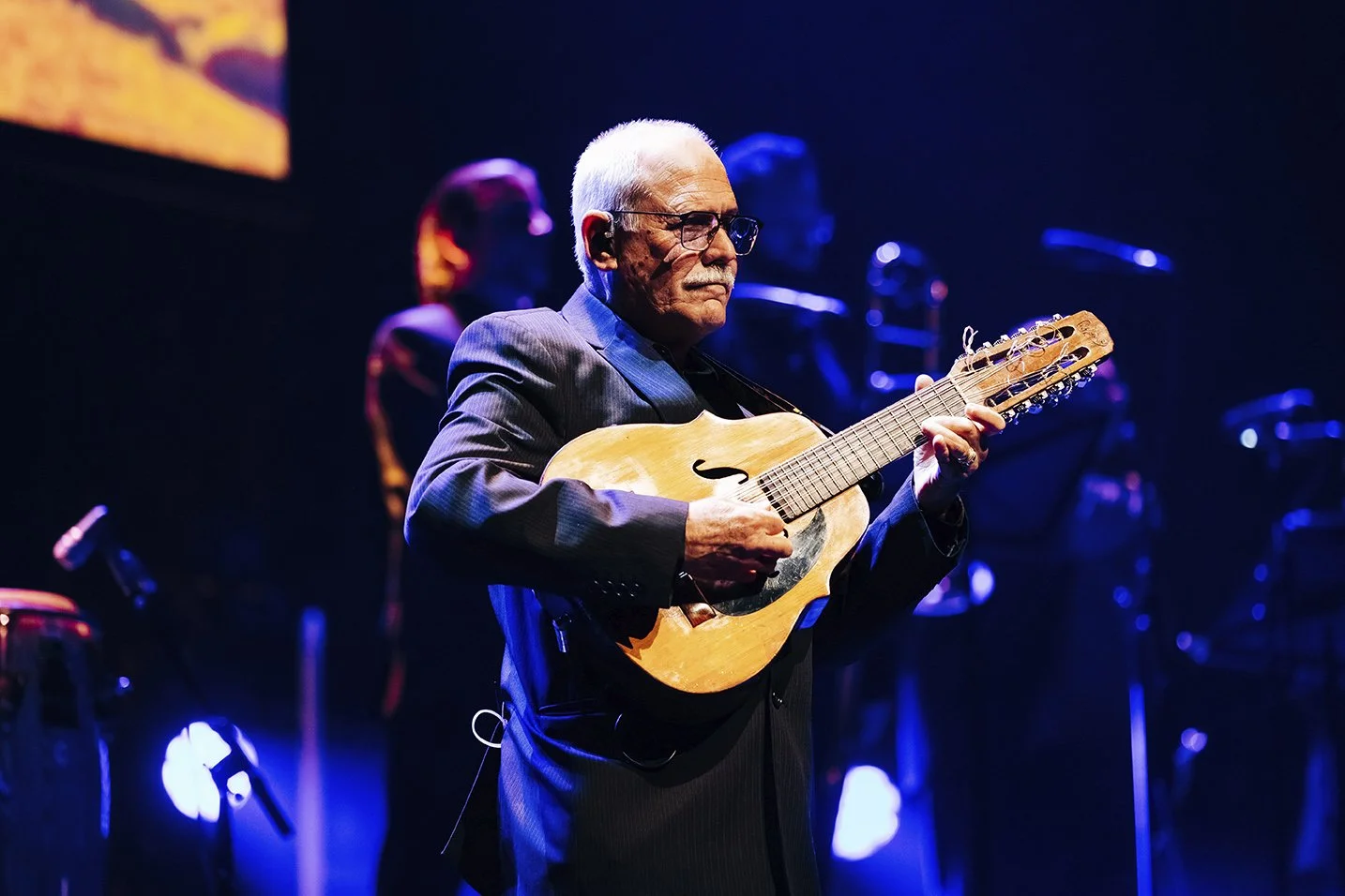 An elderly man wearing glasses and a dark suit playing a guitar on stage with blue and purple lighting. Live event and concert photography taken by Mark Gillies Photography based in Glasgow. Mark covers music events, charity balls and concerts.