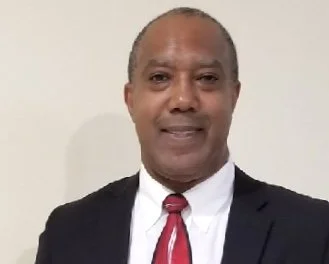Man in a suit with a red tie, smiling, standing against a plain background.