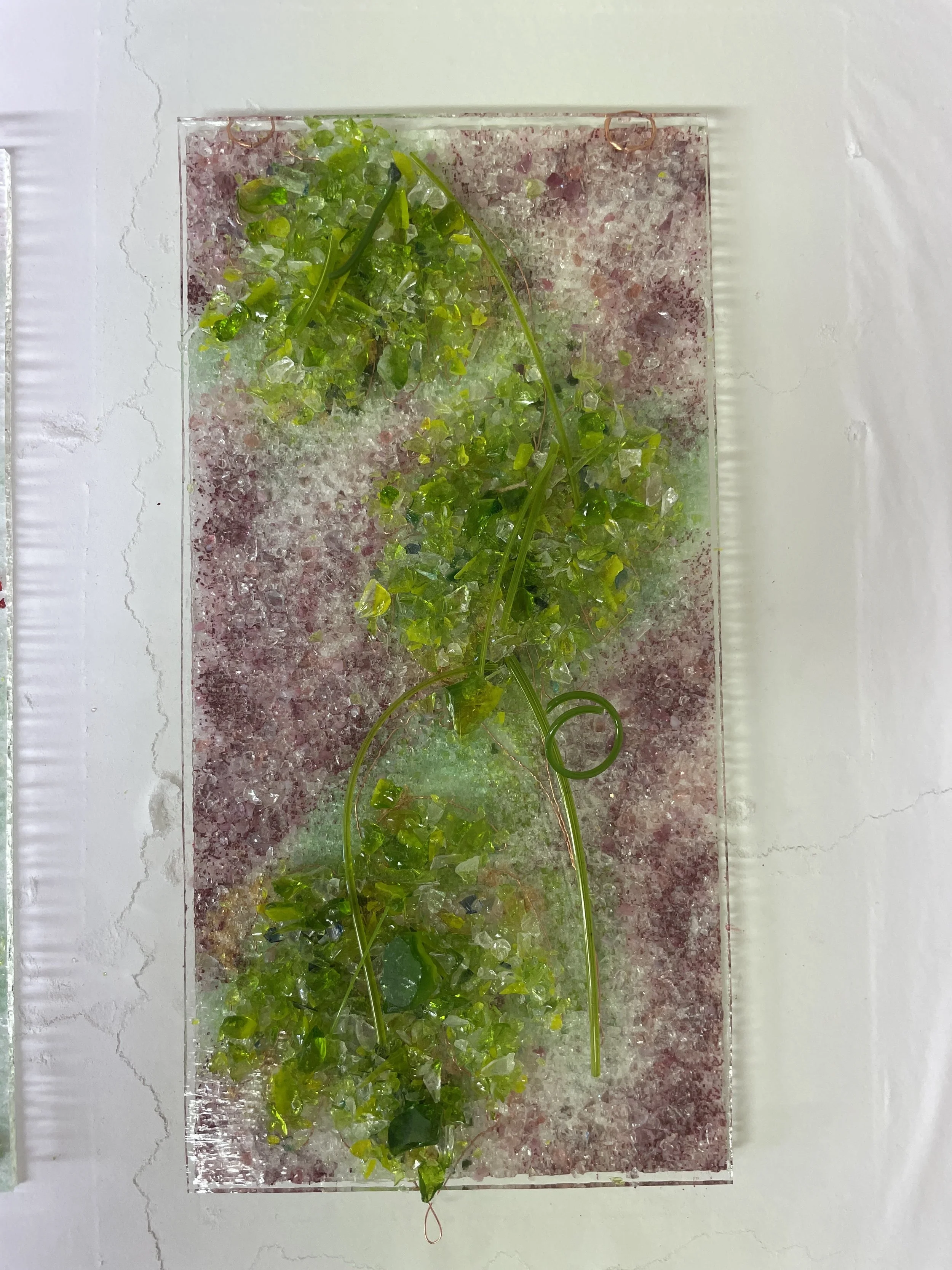 Abstract art piece featuring green glass fragments on a purple and white textured background.