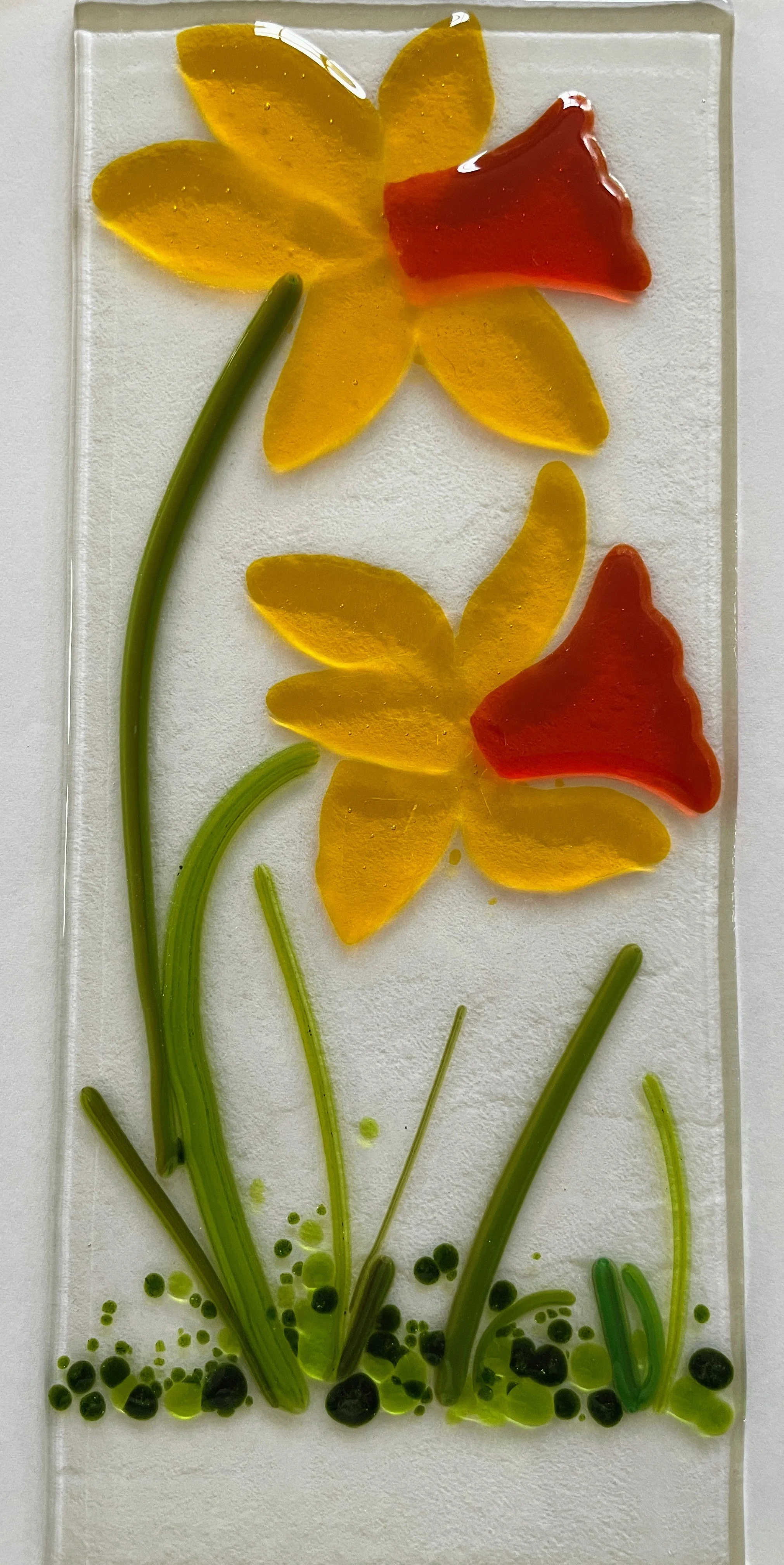 Fused glass artwork of two yellow and red daffodils with green stems and leaves