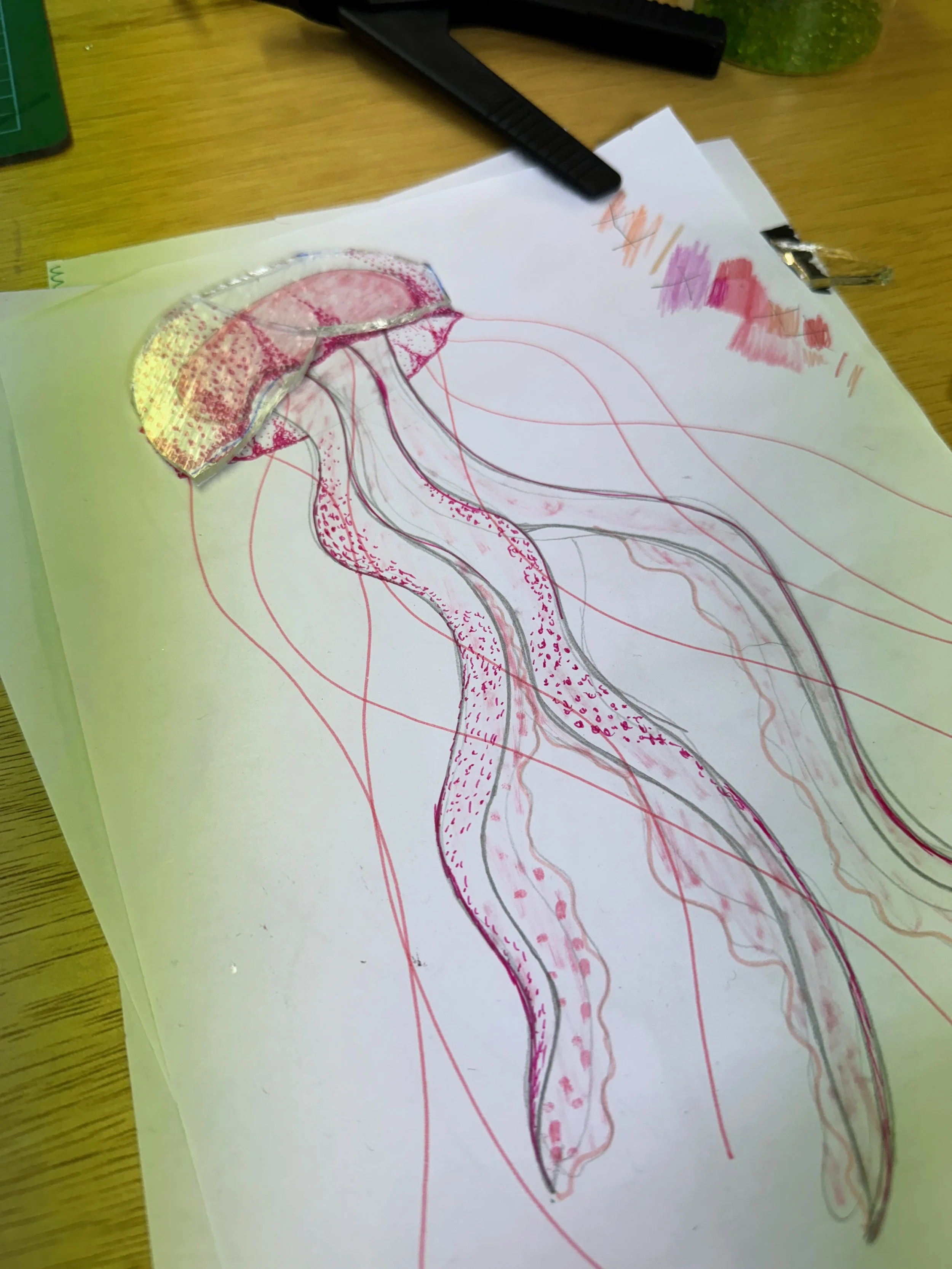 A sketch of a jellyfish on paper, with colored pencils and markers on a wooden table.