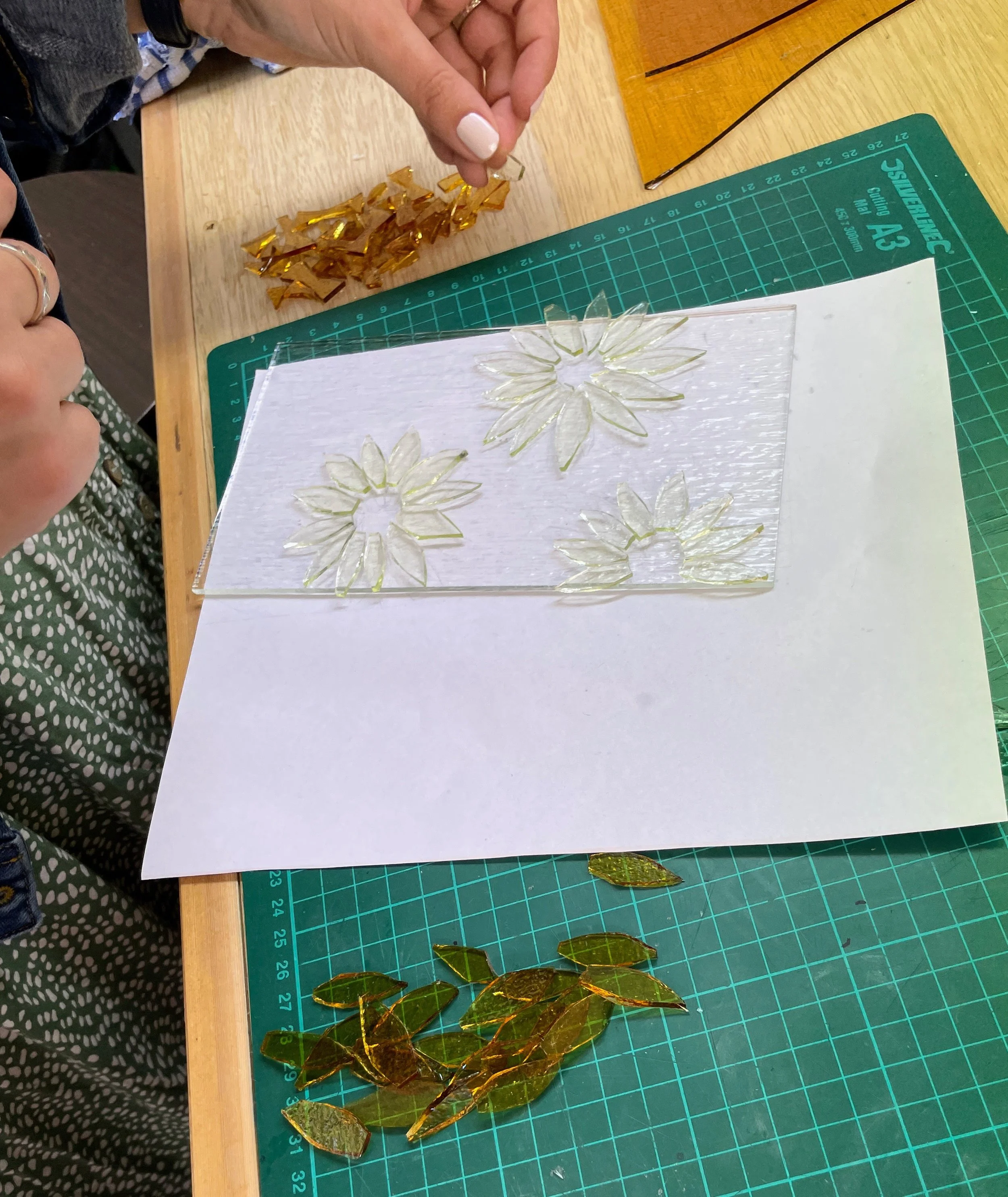 Person arranging stained glass pieces on a crafting surface with floral patterns