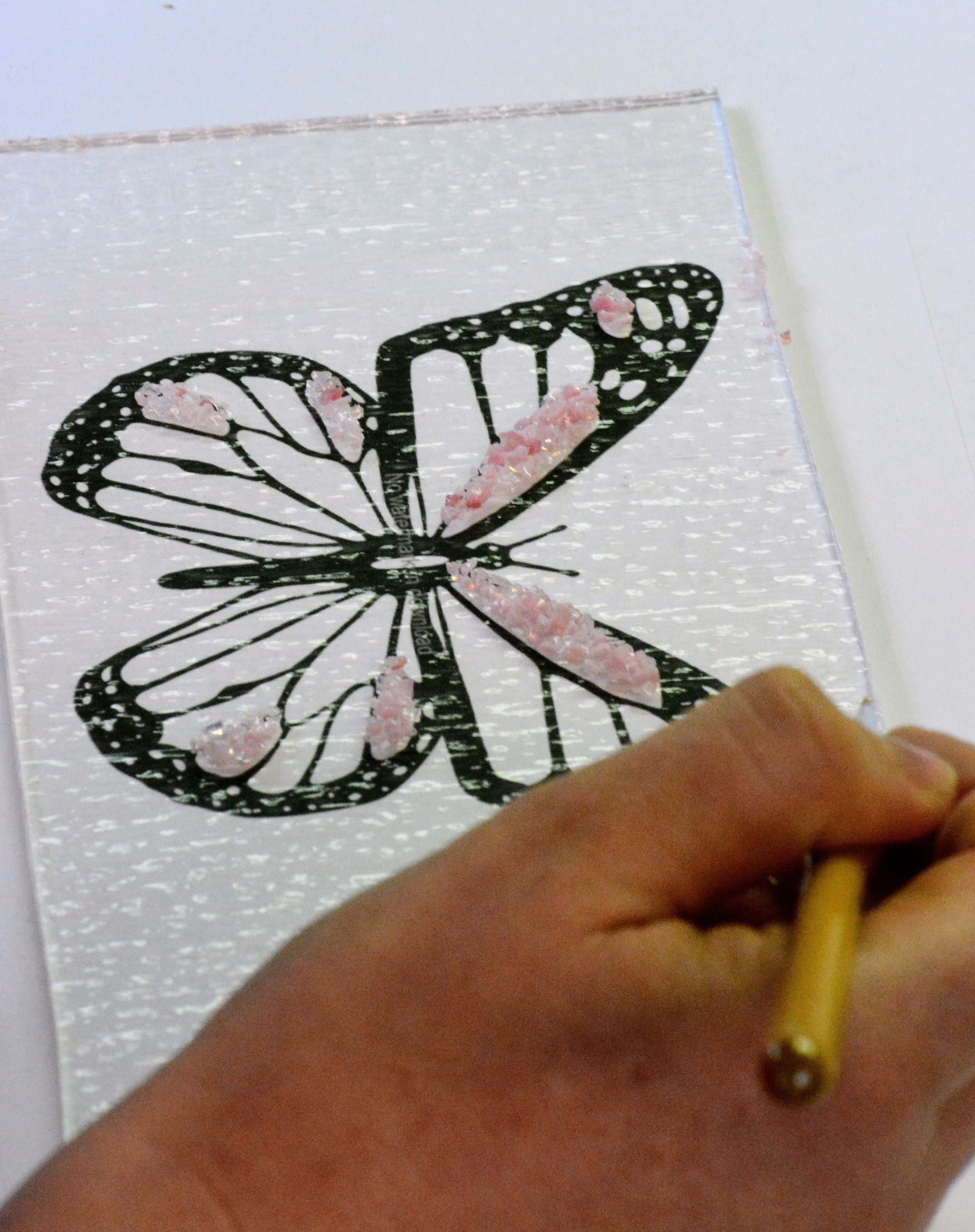 Hand drawing a butterfly with a pencil and textured pink accents on a paper