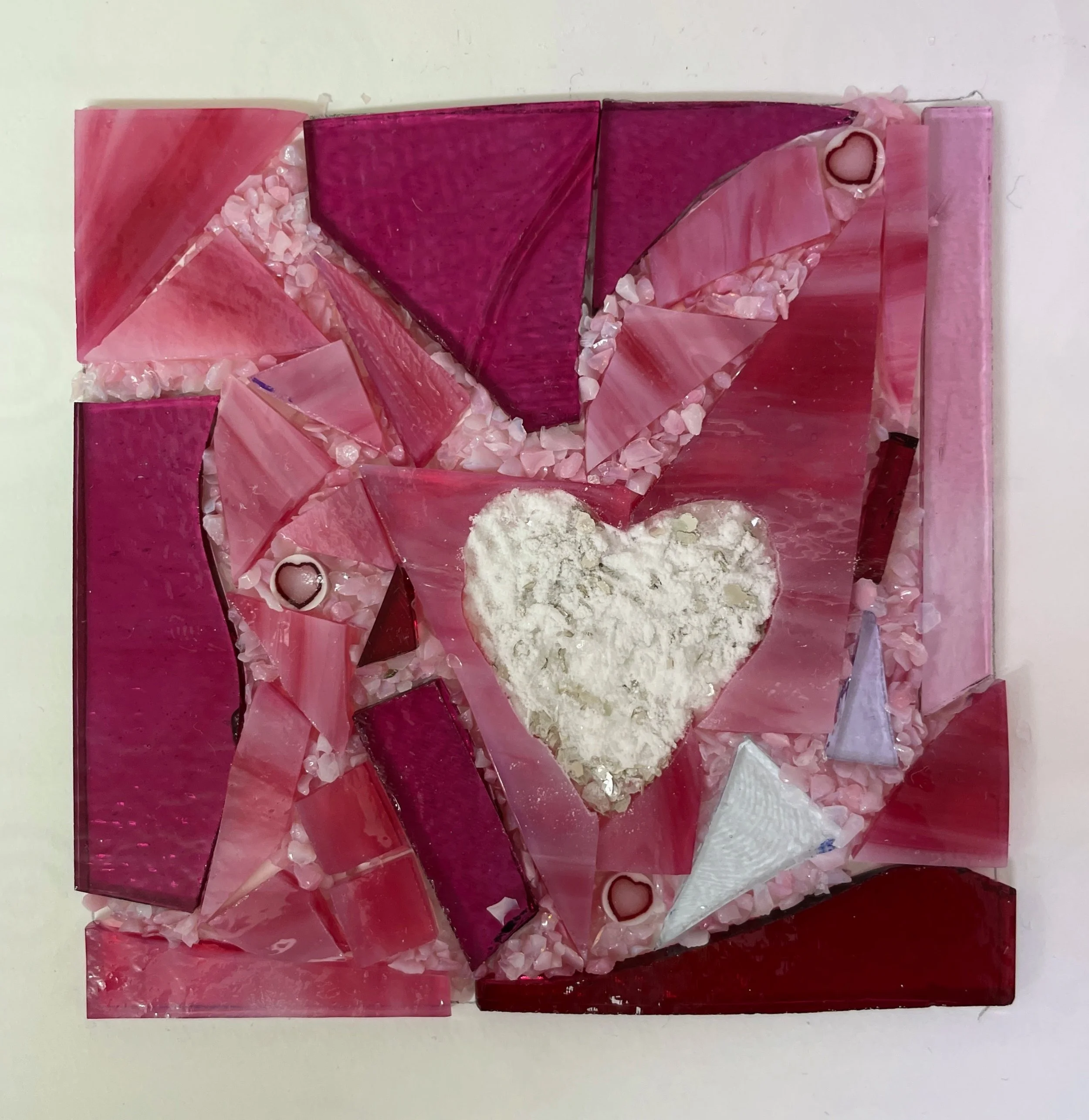 Mosaic artwork with pink and red glass pieces surrounding a white heart shape.