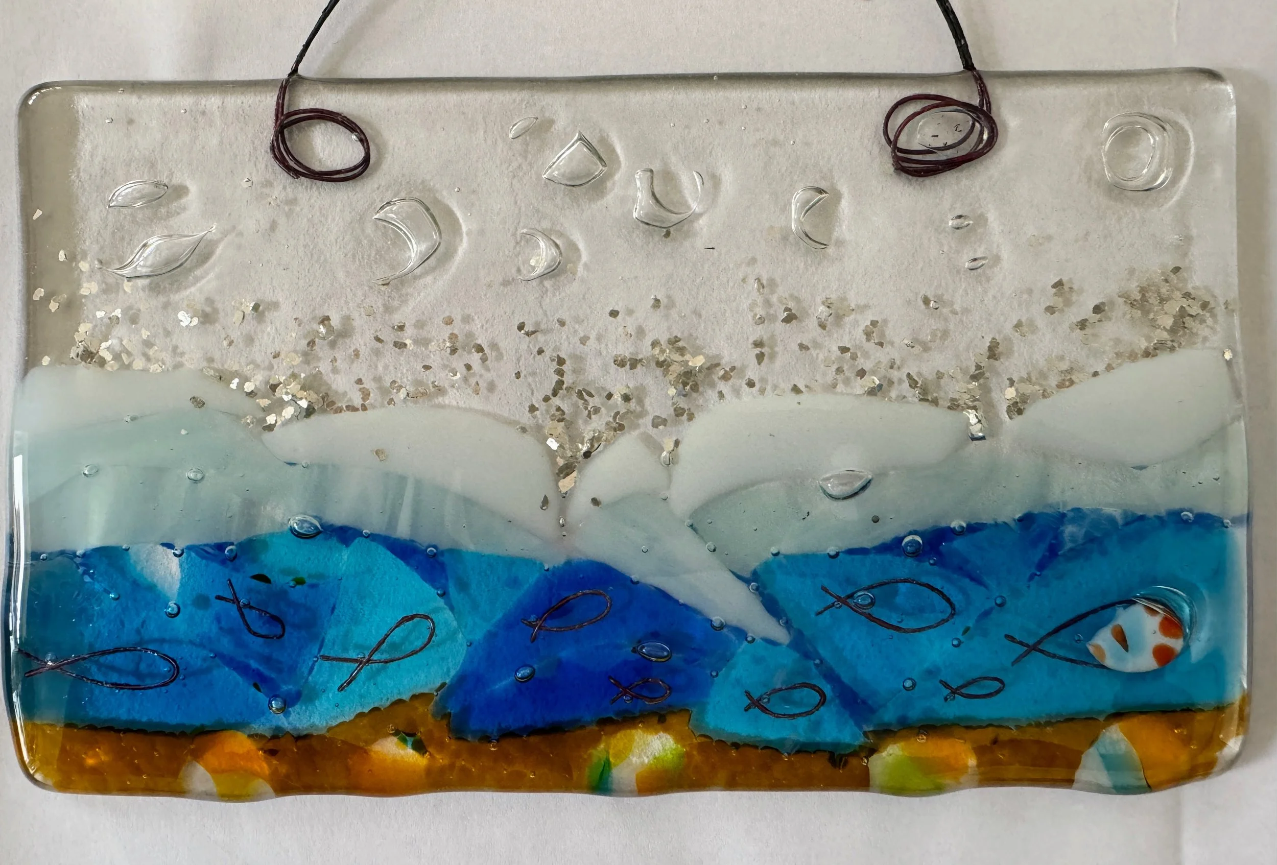 Decorative fused glass panel depicting an underwater scene with abstract fish patterns and bubble textures, featuring layers of blue, white, and amber tones.