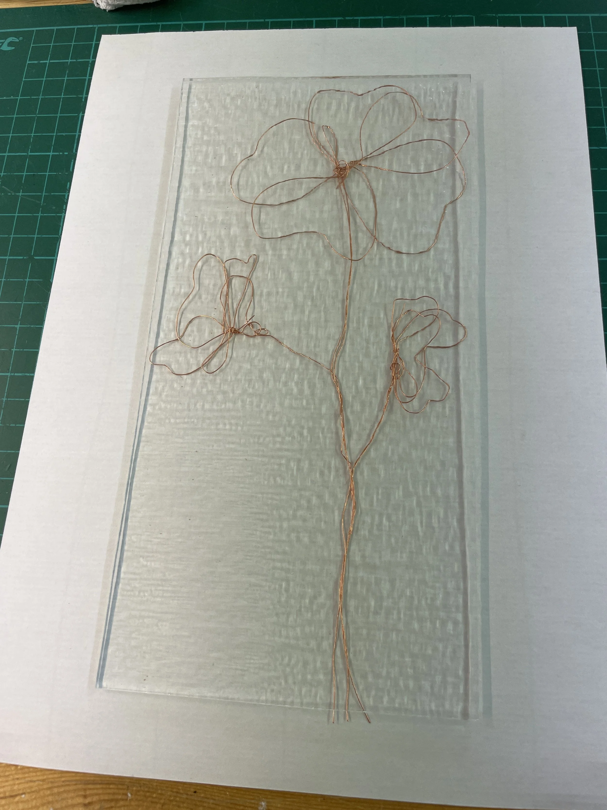 Wire art of flowers on textured paper, placed on a green cutting mat.