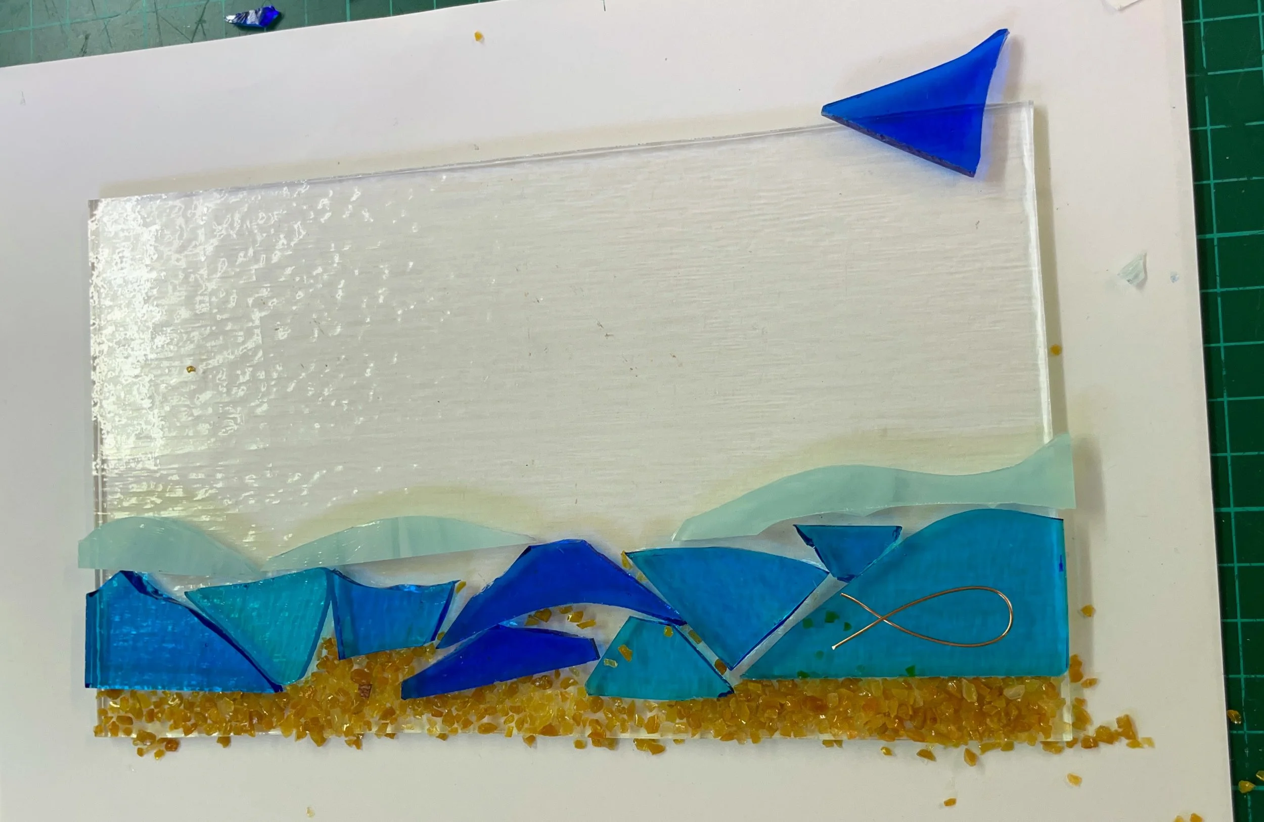 Glass artwork depicting a beach scene with blue waves and a blue sailboat.