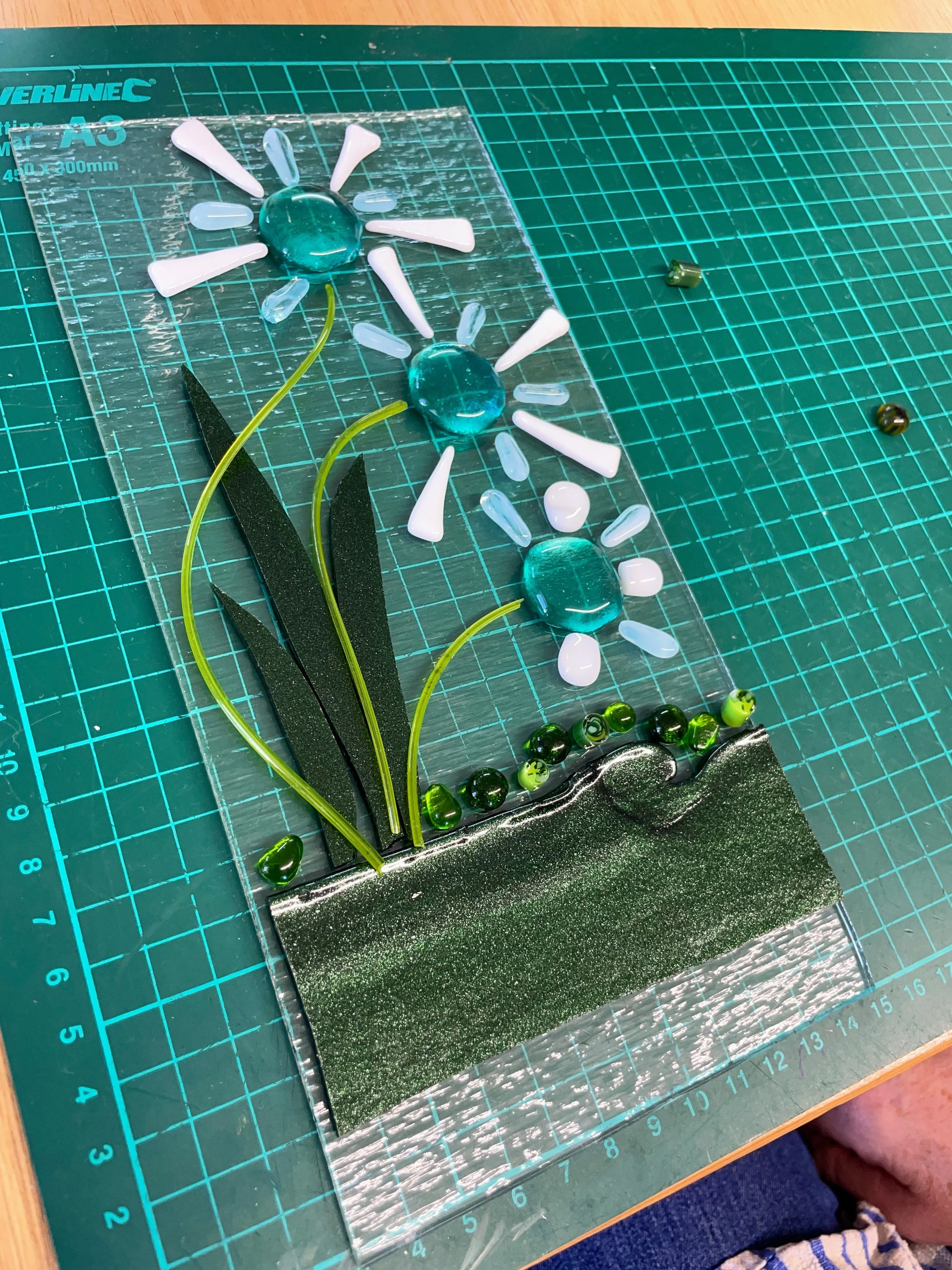 Glass art project with blue and white flowers on a green cutting mat