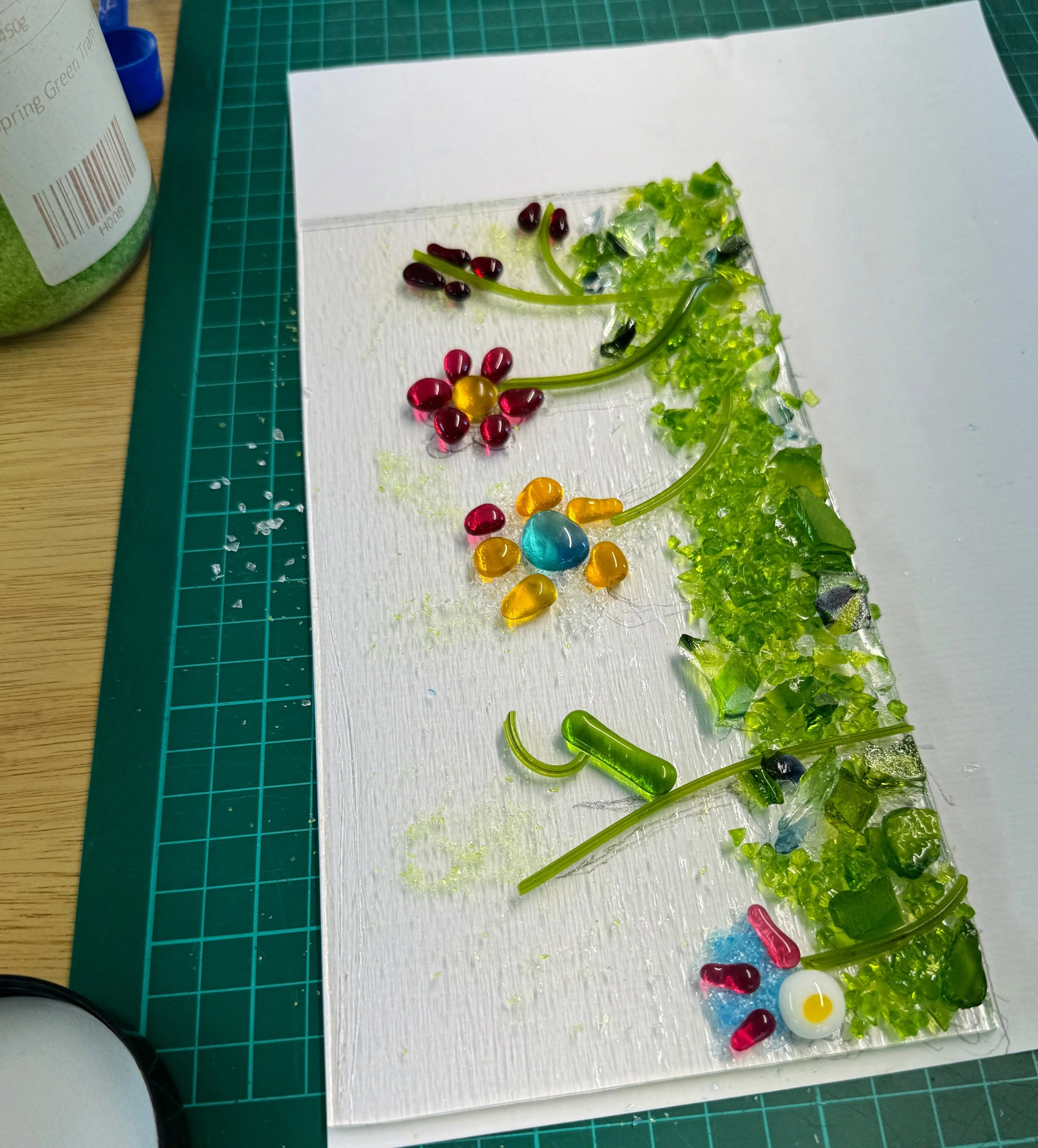 Colorful glass mosaic art of flowers on a white board, placed on a cutting mat.