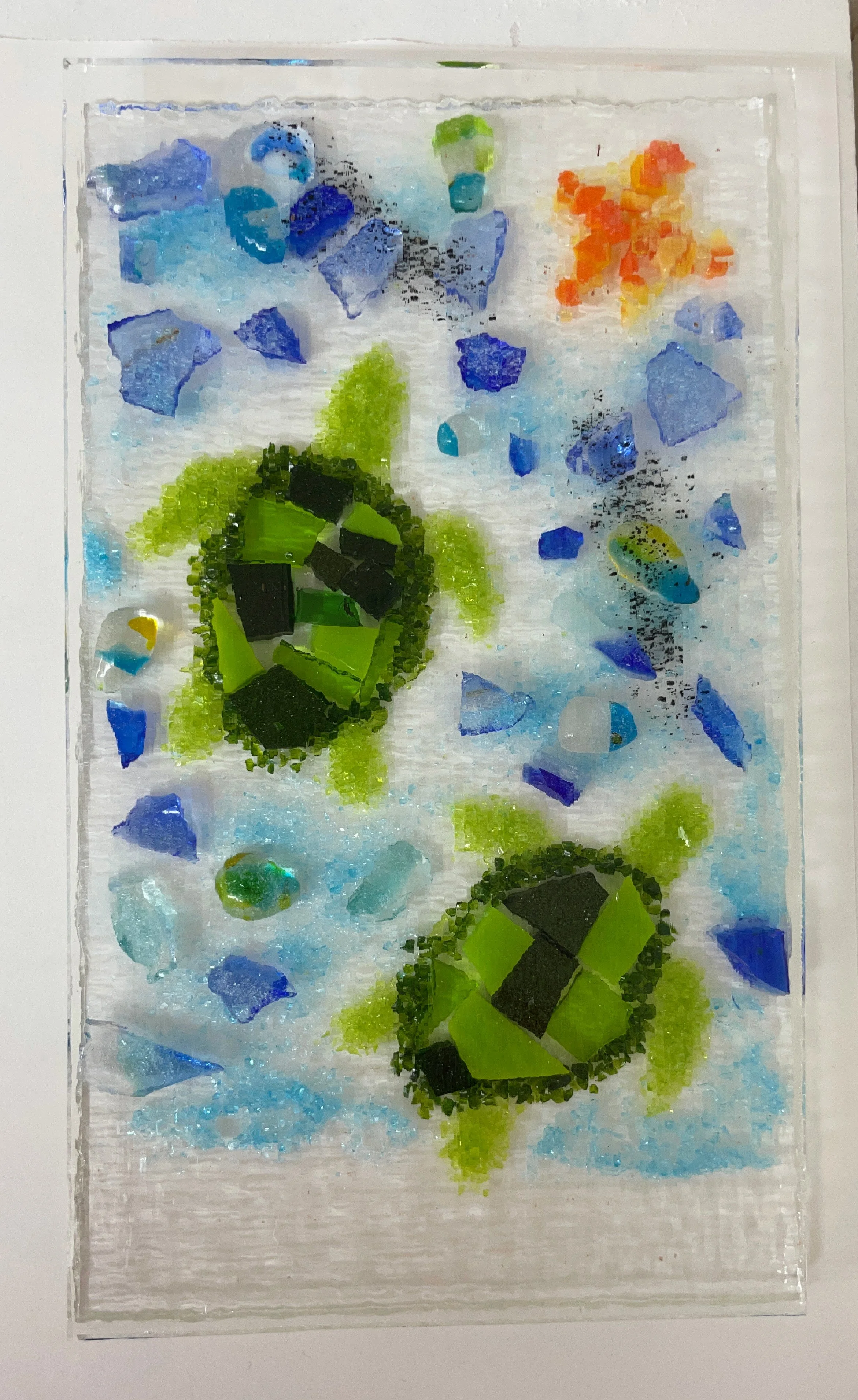 Glass art featuring two green sea turtles swimming surrounded by blue, green, and orange fragments