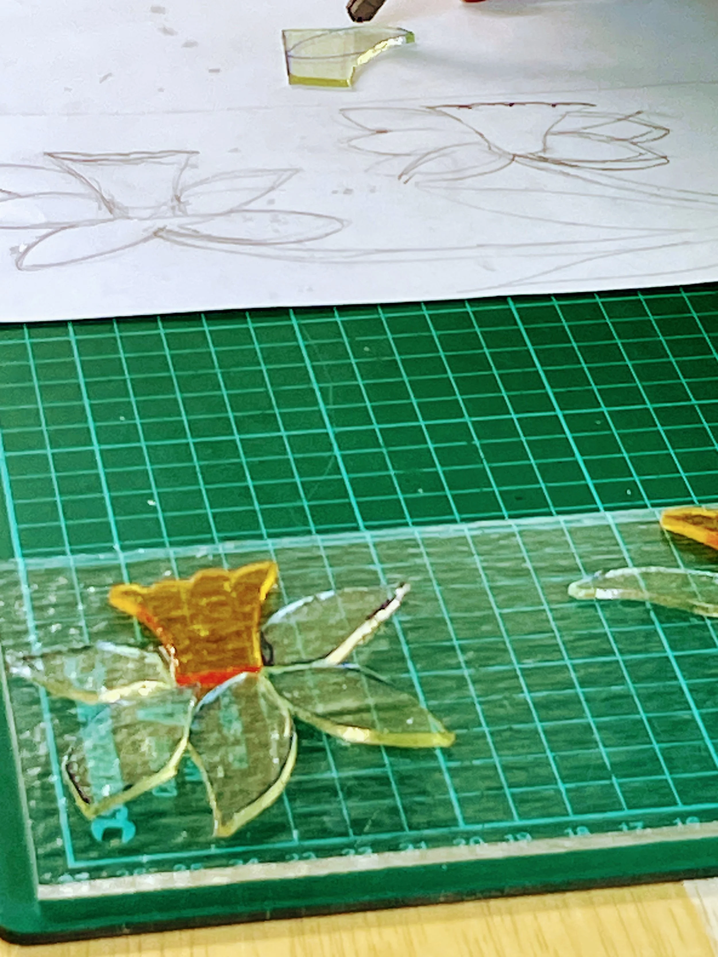Close-up of a stained glass project featuring flower designs on a cutting mat.