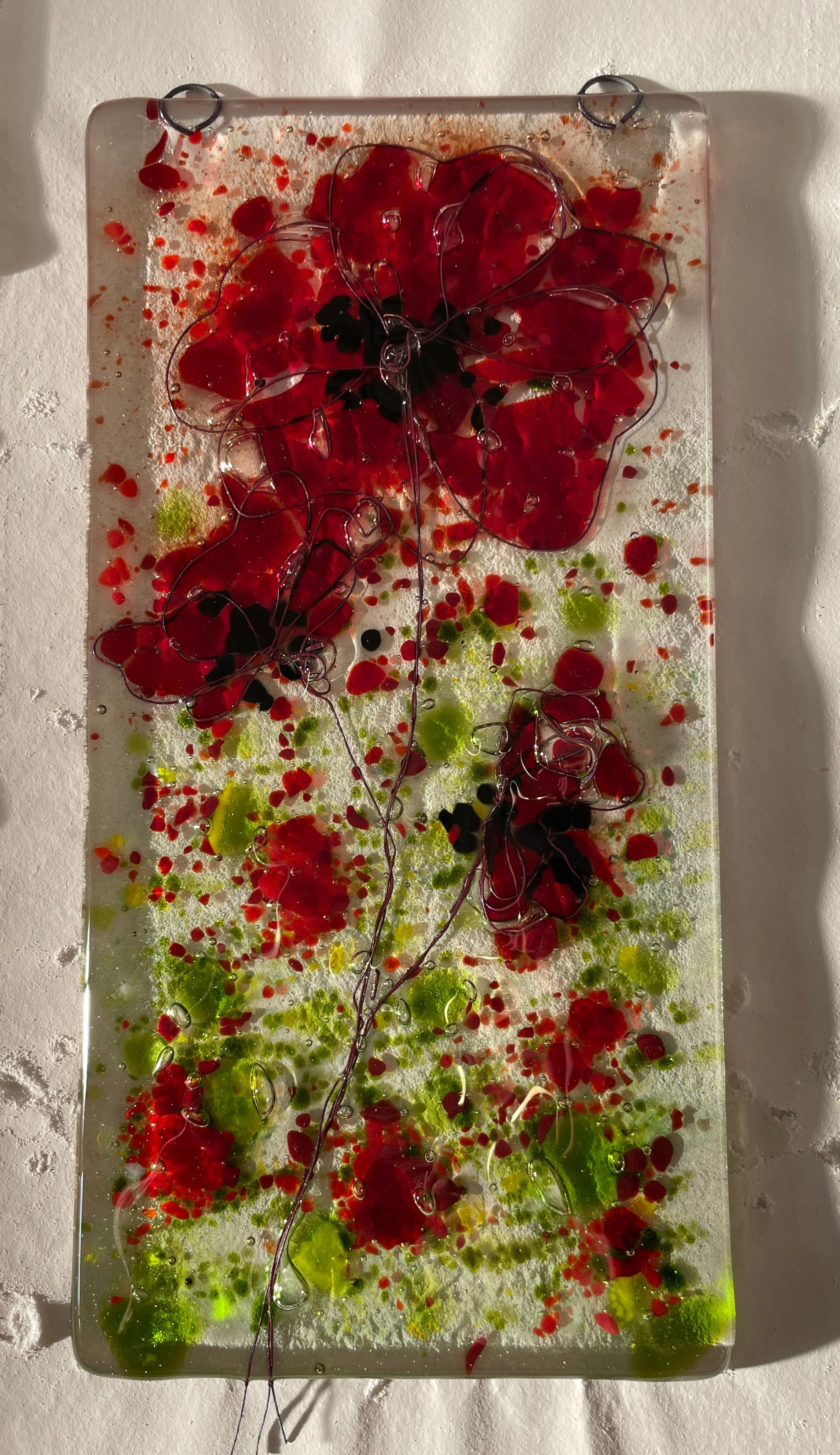 Glass art panel featuring abstract red and green floral design with wire accents against a textured background.
