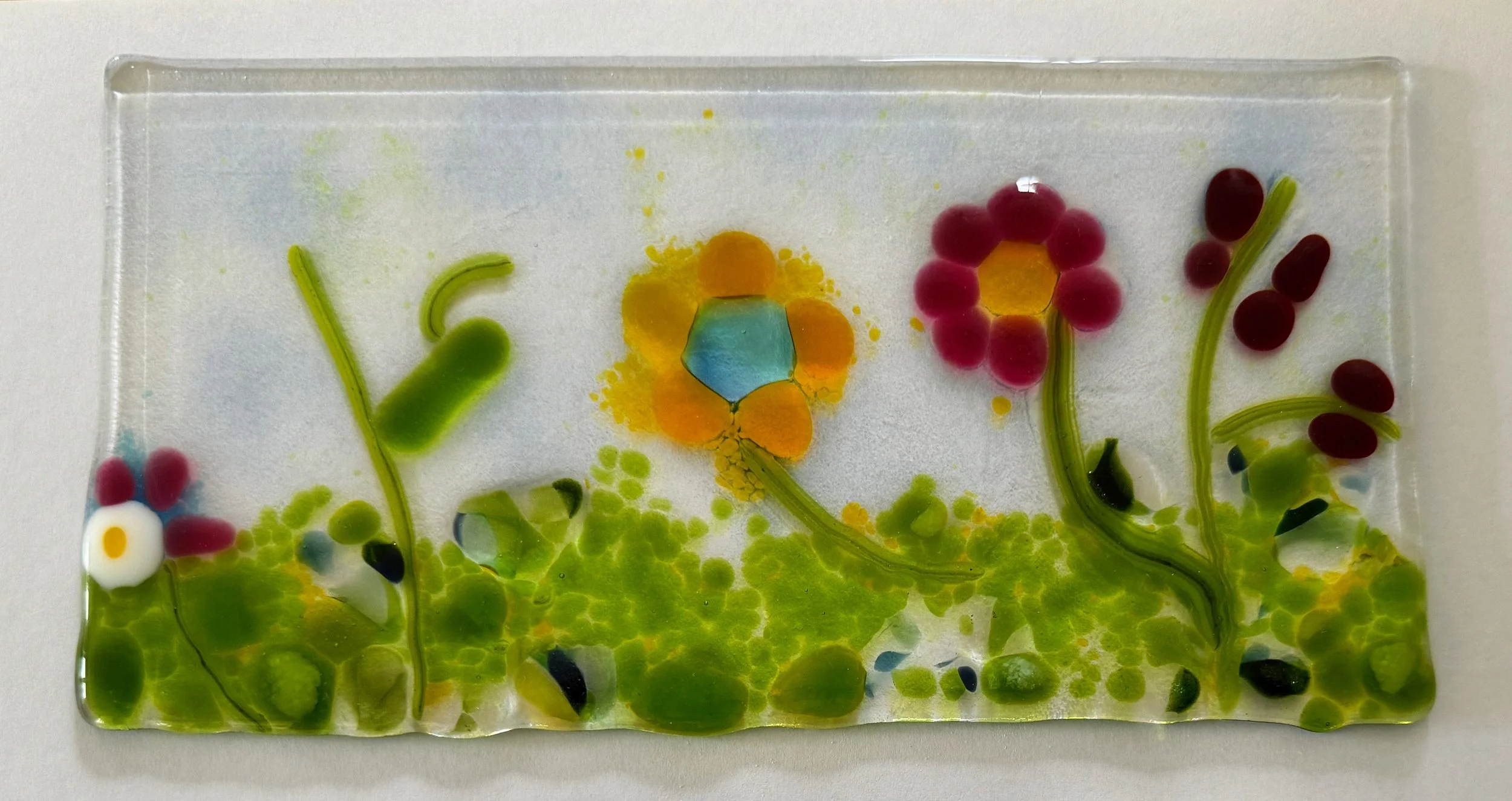 Decorative glass art piece featuring colorful flowers and green foliage.