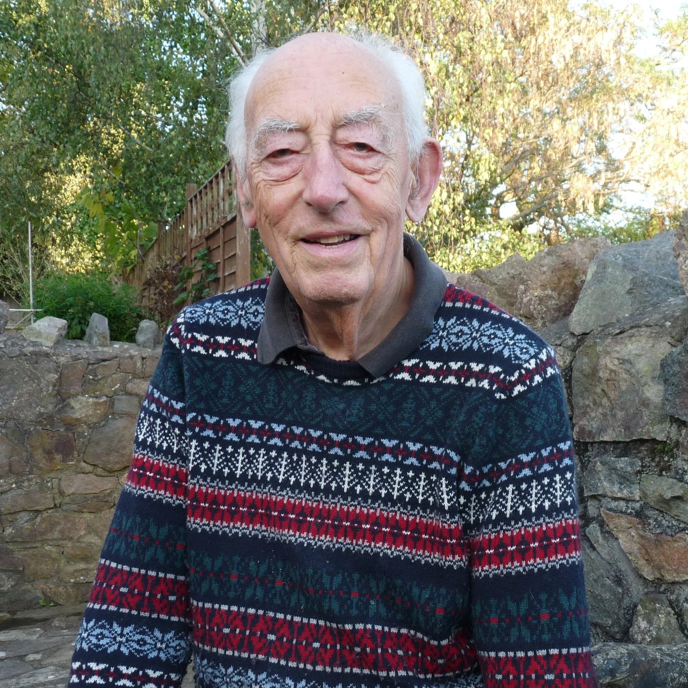 Portrait of an elderly man with white hair, smiling, sitting in front of a green curtain.