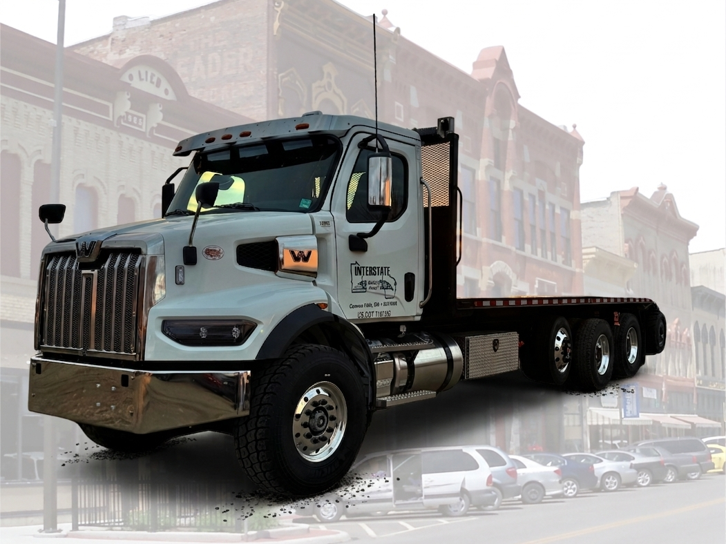 Interstate Building Supply flatbed truck delivering to downtown Faribault, MN, with the historic Lieb Block and Central Avenue buildings in the background.