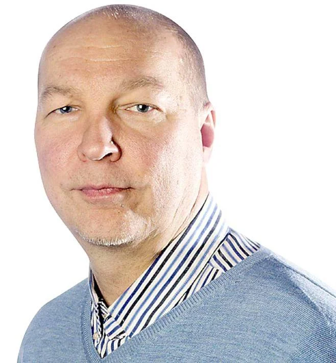 Kaljuuntuva mies katsoo kameraan, raidallinen kauluspaita ja harmaa paita.