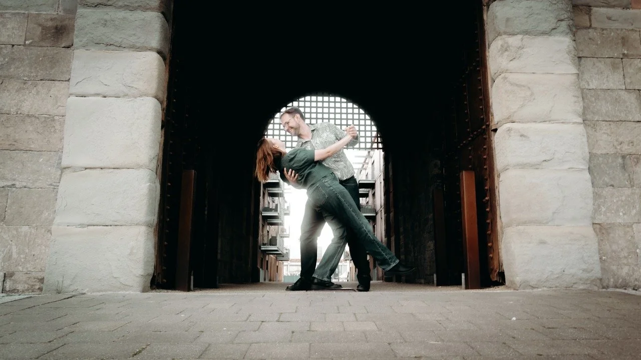 A couple dancing in an archway with stone walls and a city street visible in the background.