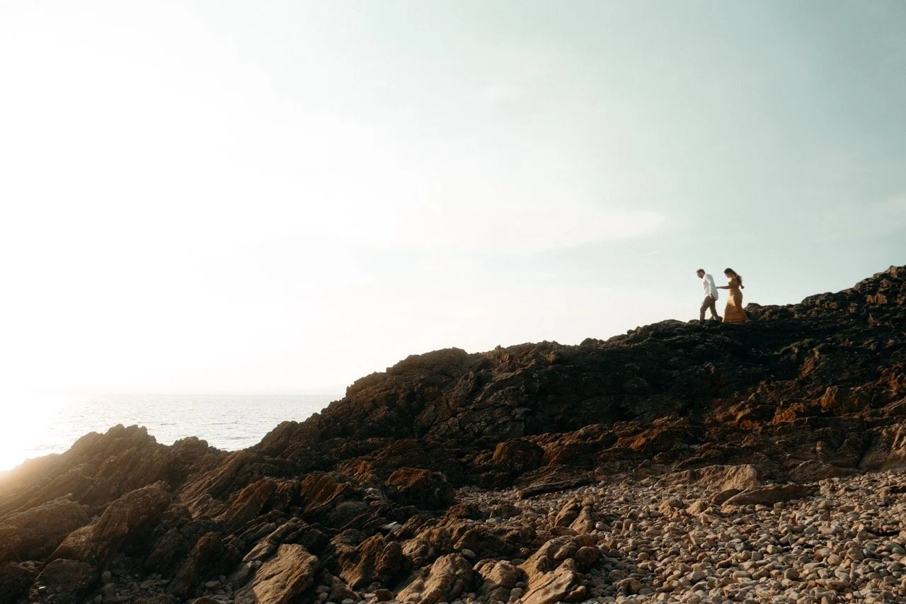 A couple walking along a rocky beach during sunset.
