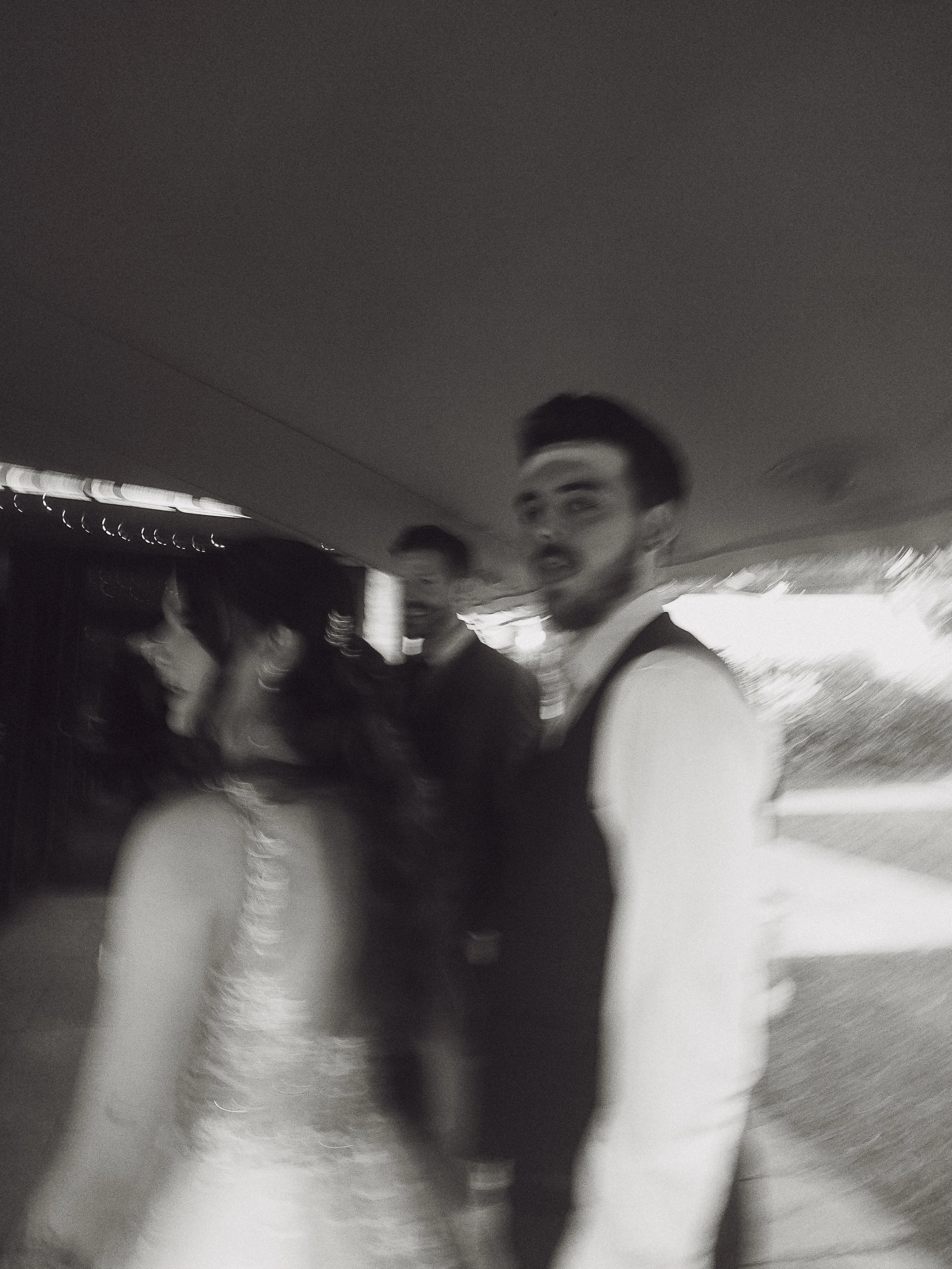 Black and white photo of a woman in a wedding dress and two men, one in a dress shirt and vest, and the other in a dark suit, standing together in an indoor setting.