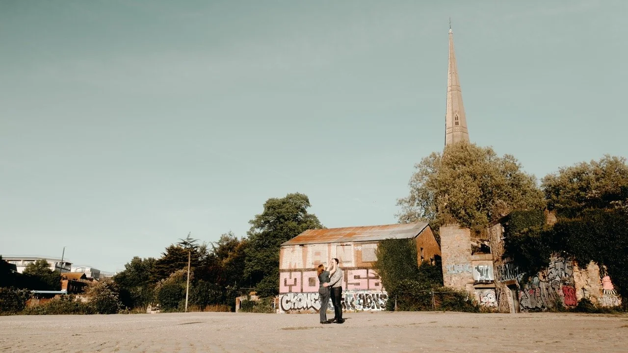 A couple dancing in an open area with an old graffiti-covered building and a tall church steeple in the background.