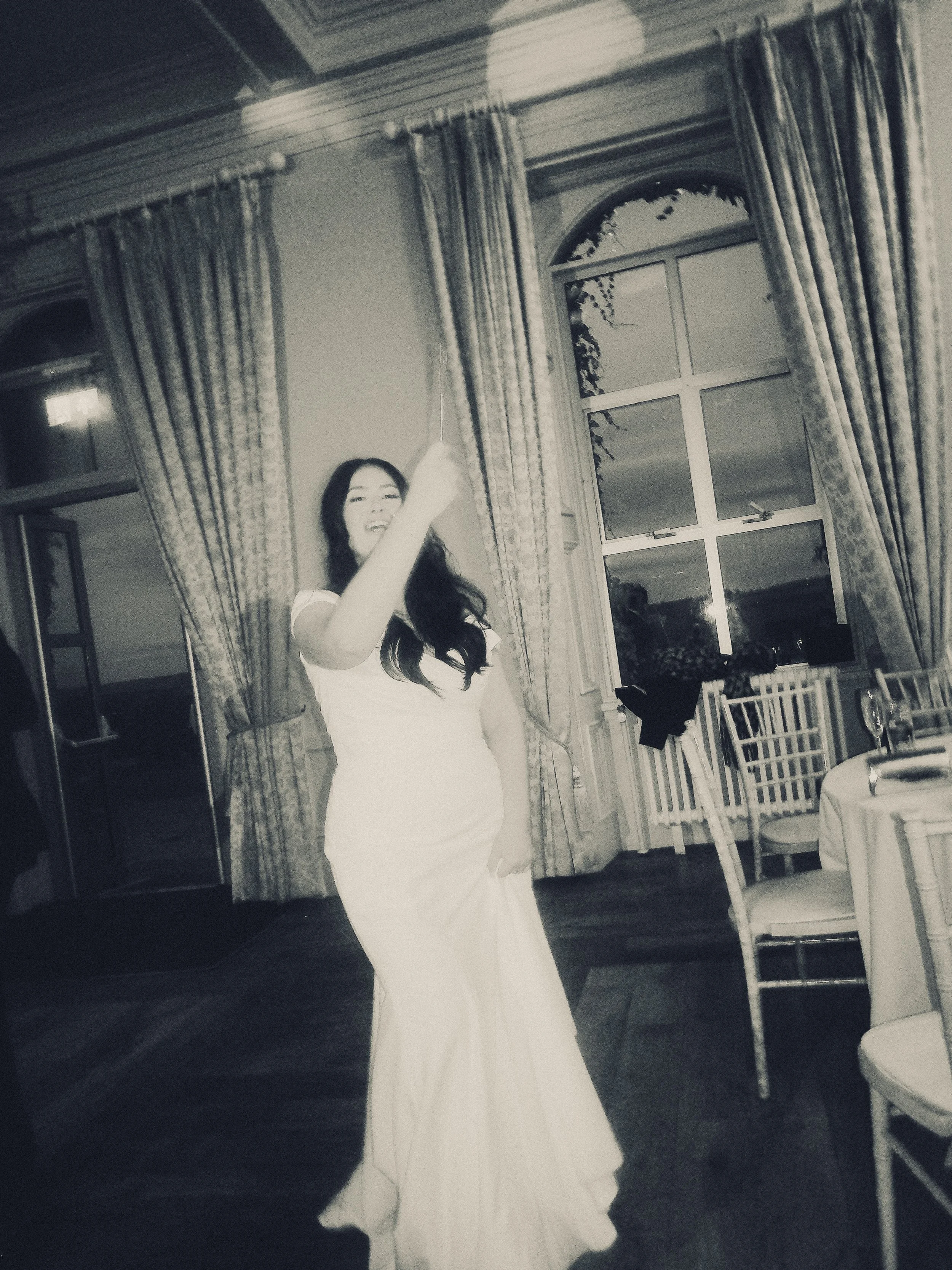 A woman in a white dress celebrating with a sparkler in a decorated indoor venue.