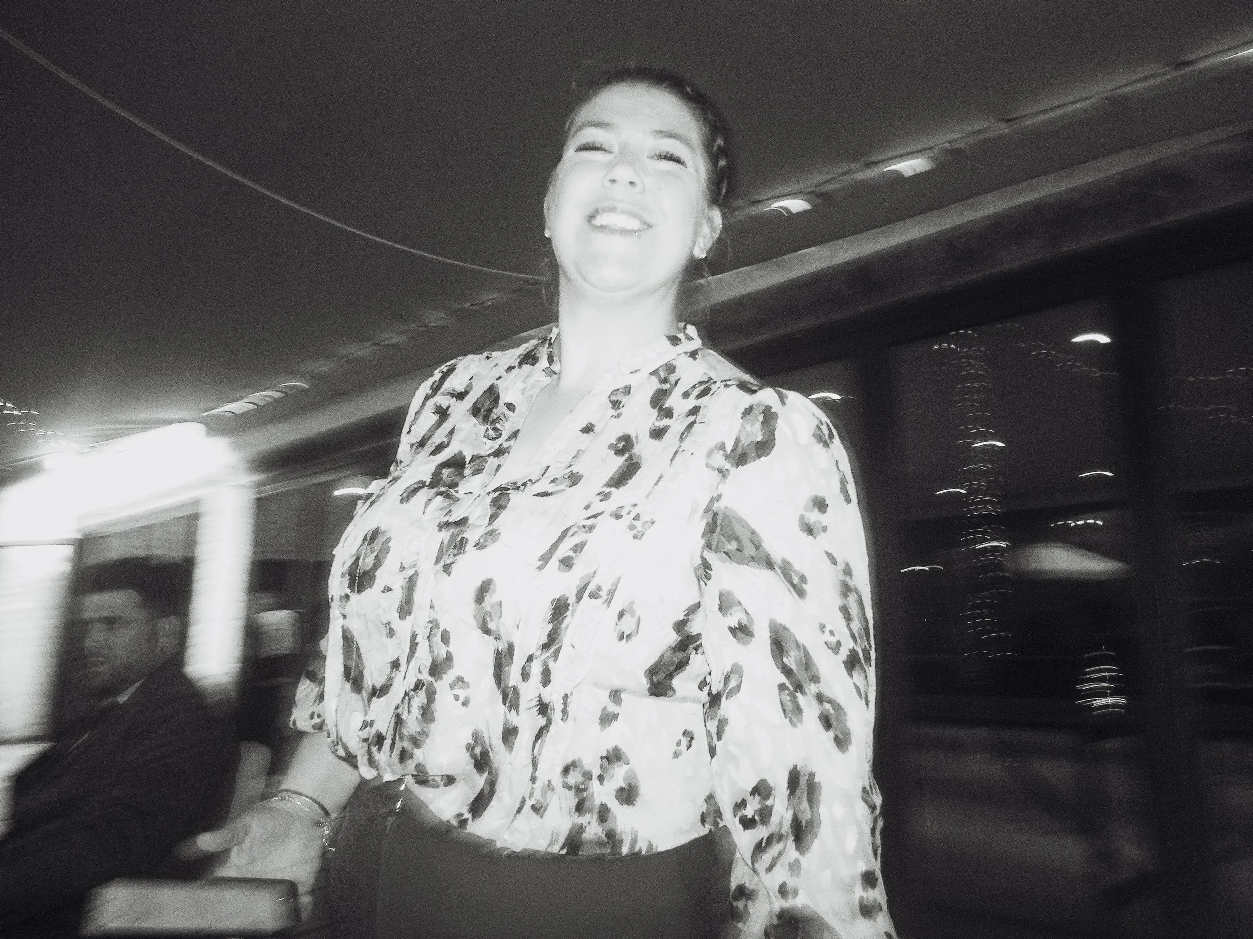 A woman smiling and wearing a leopard print top, standing near a bus at night.