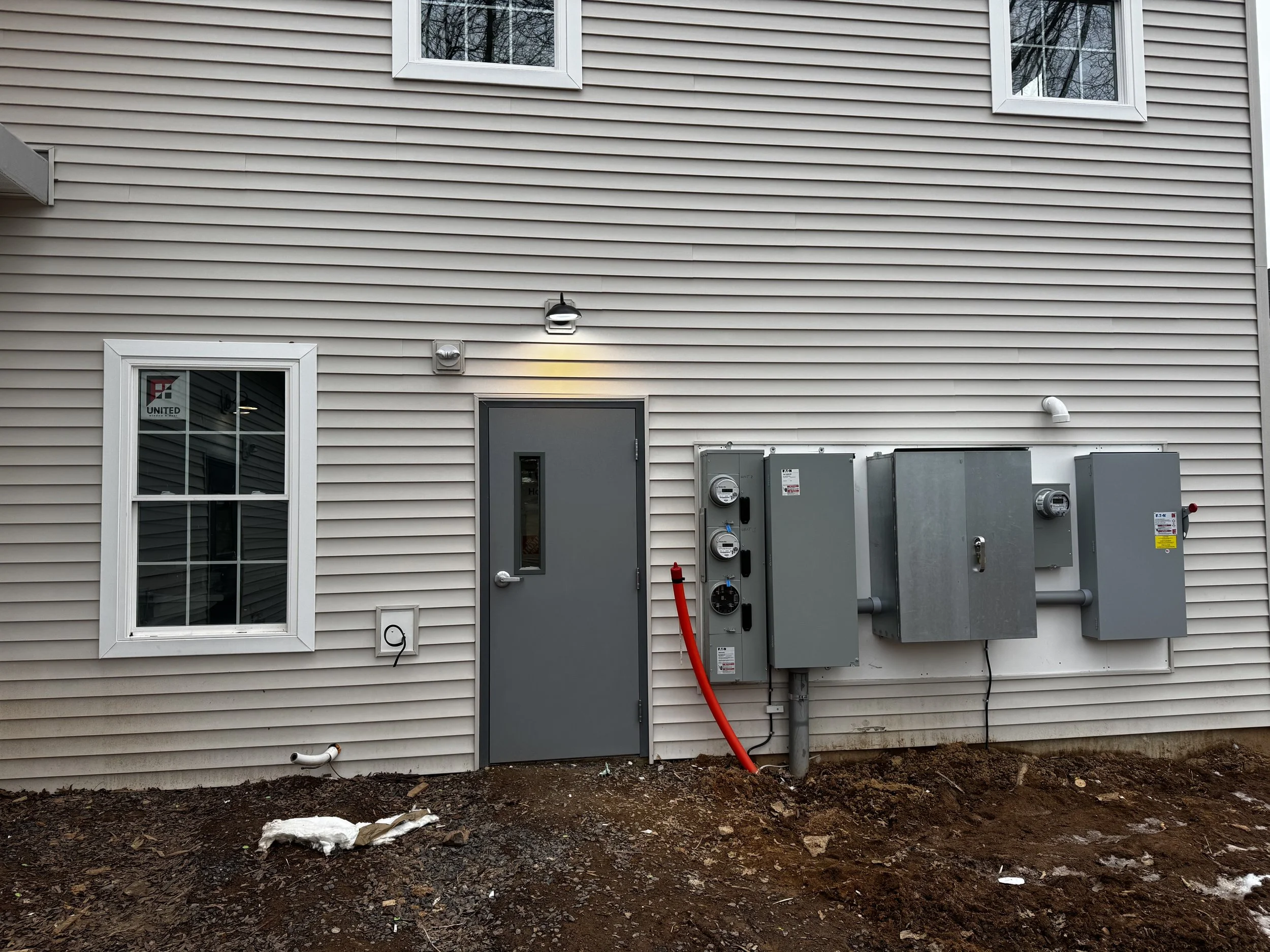 Electrical panels and conduit pipes mounted on a wall in a basement or utility room.