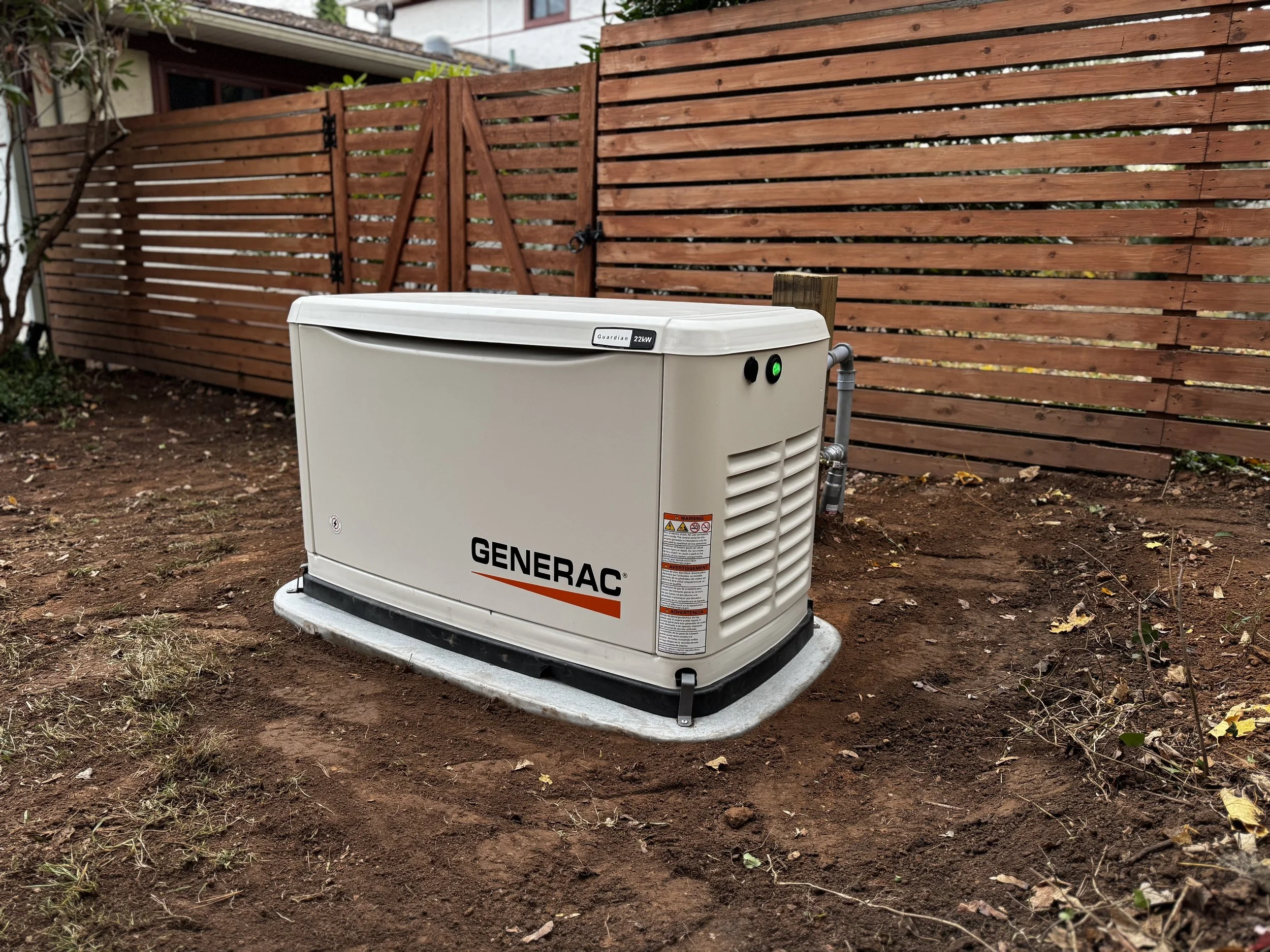 Technician working on outdoor HVAC or electrical equipment near a white building with trees and parked cars in the background.