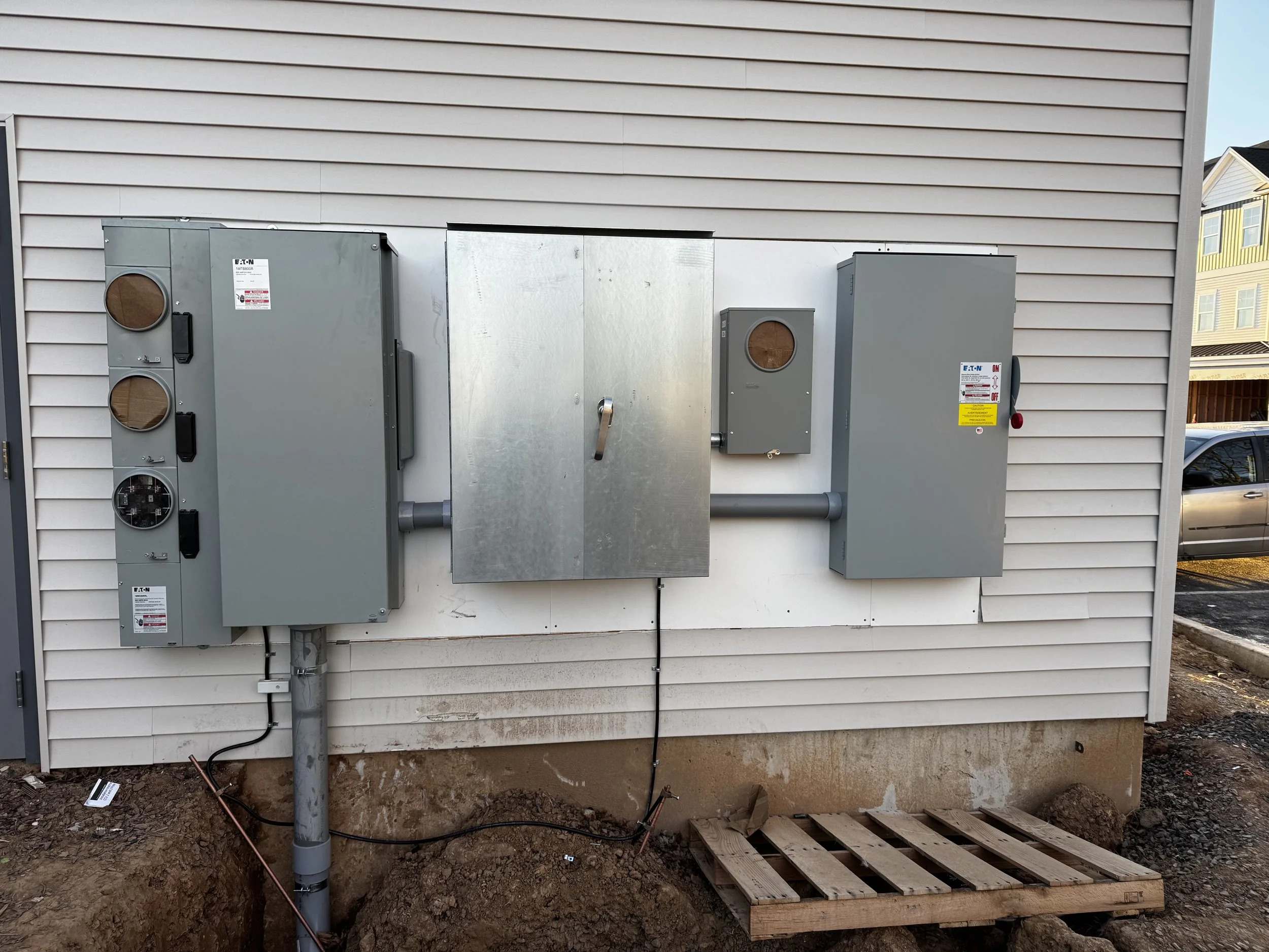 Electrical panels and conduit pipes mounted on a wall in a basement or utility room.