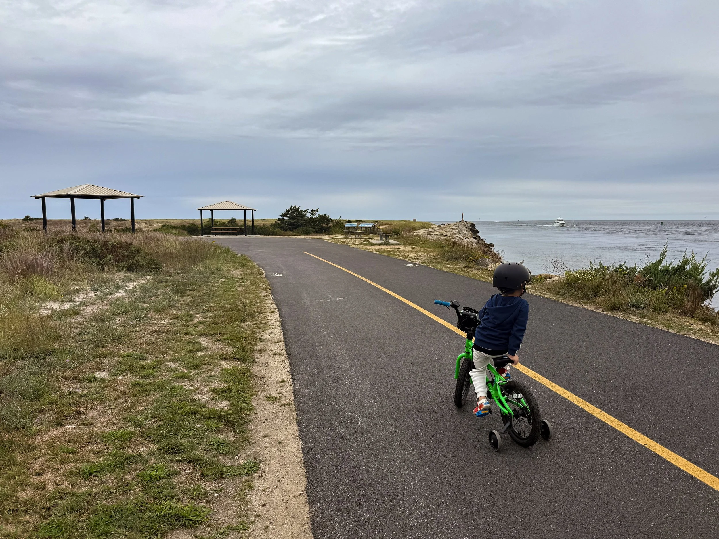 Little boy riding a green bike along the Cape Cod Canal at Scusset Beach