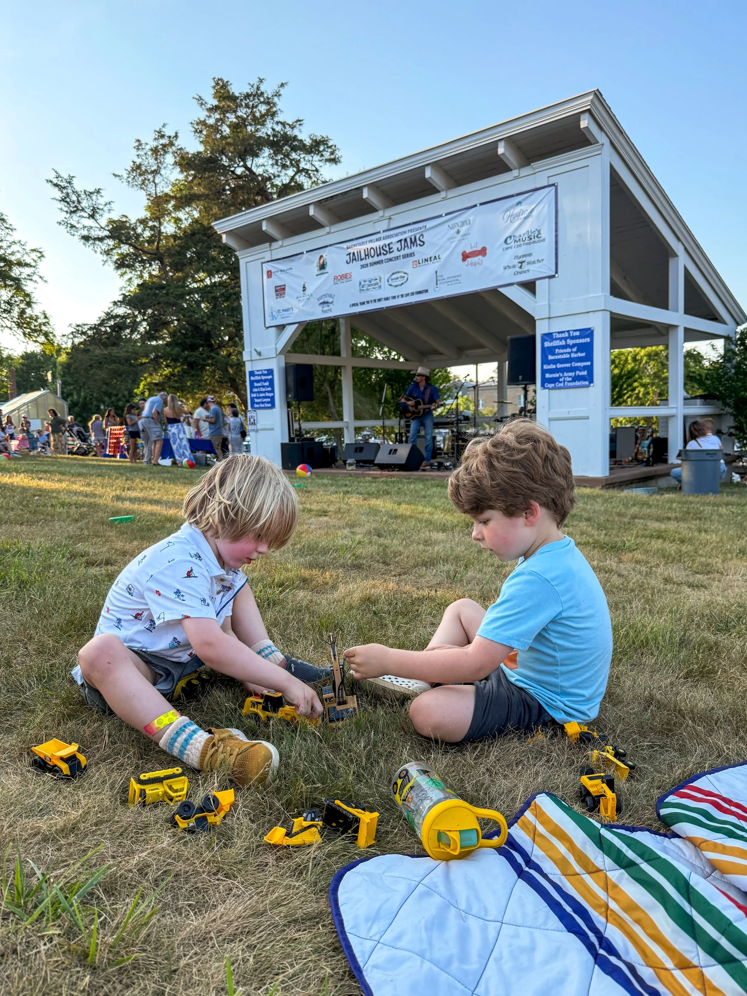Two little boys playing with construction trucks on the lawn at Jailhouse Jams in Barnstable Village