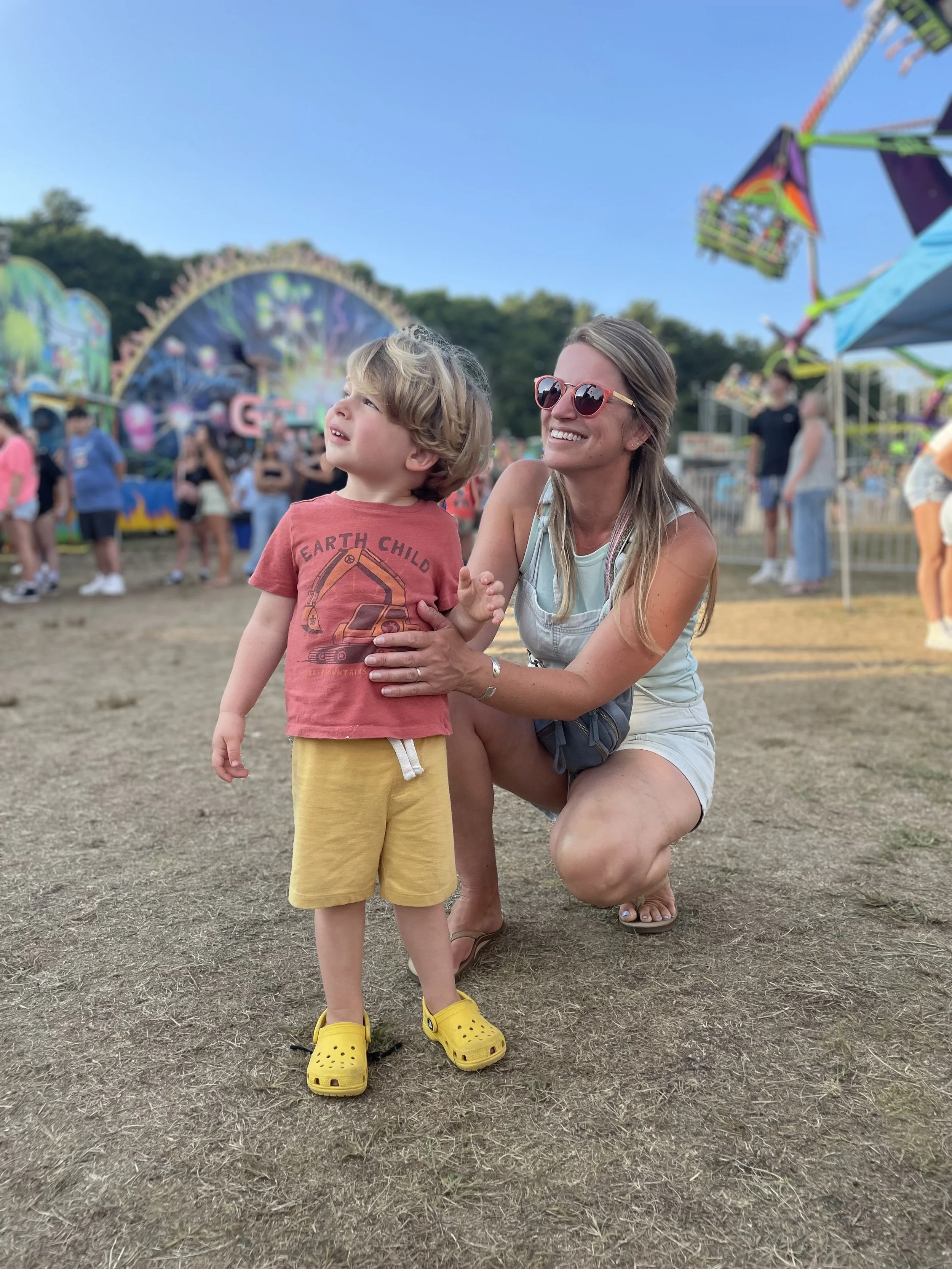 A mother and son in summer clothes watching the carnival rides at the Barnstable County Fair on Cape Cod