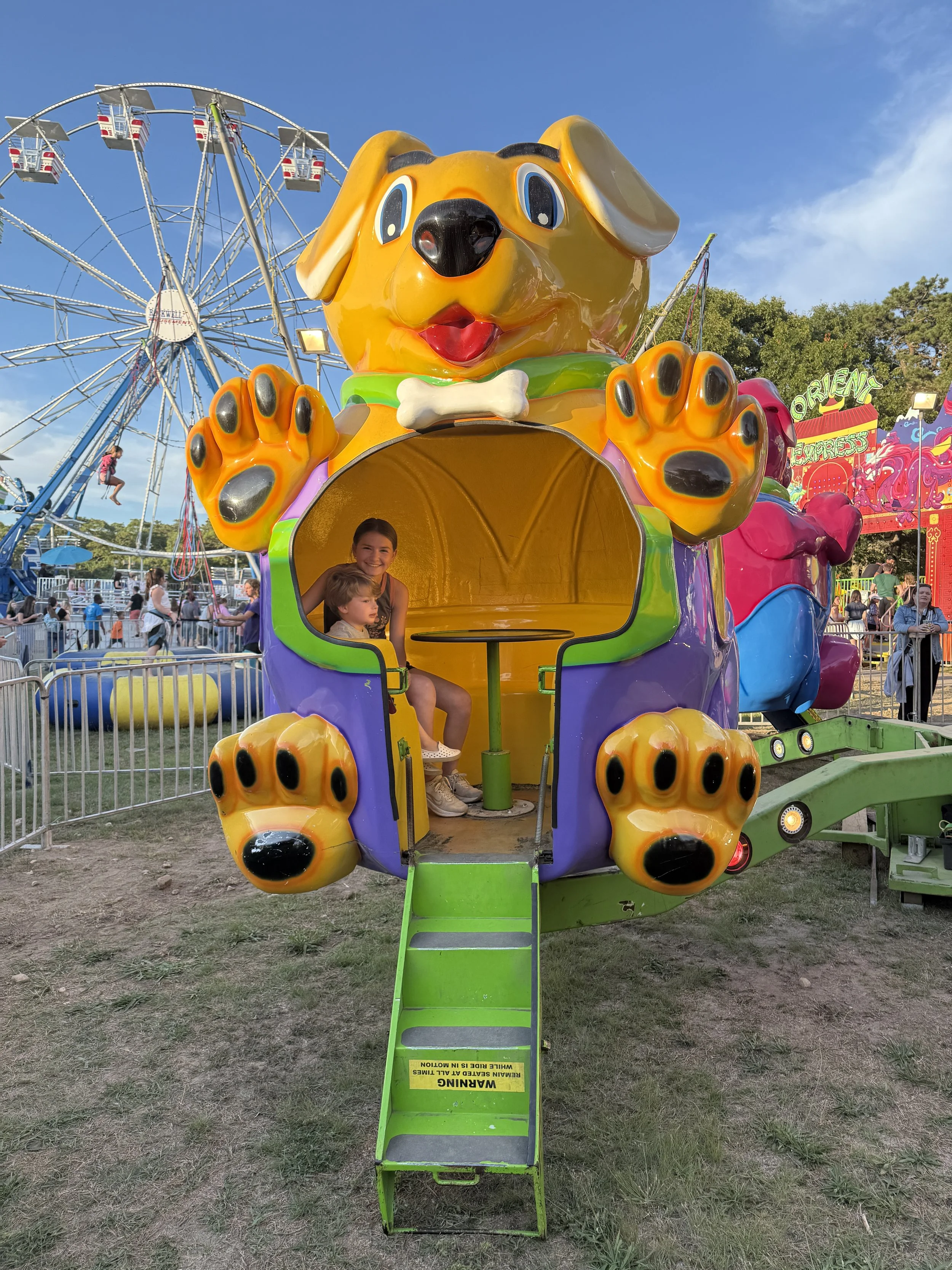 Two young kids on a yellow dog-shaped carnival ride at the Barnstable County Fair on Cape Cod