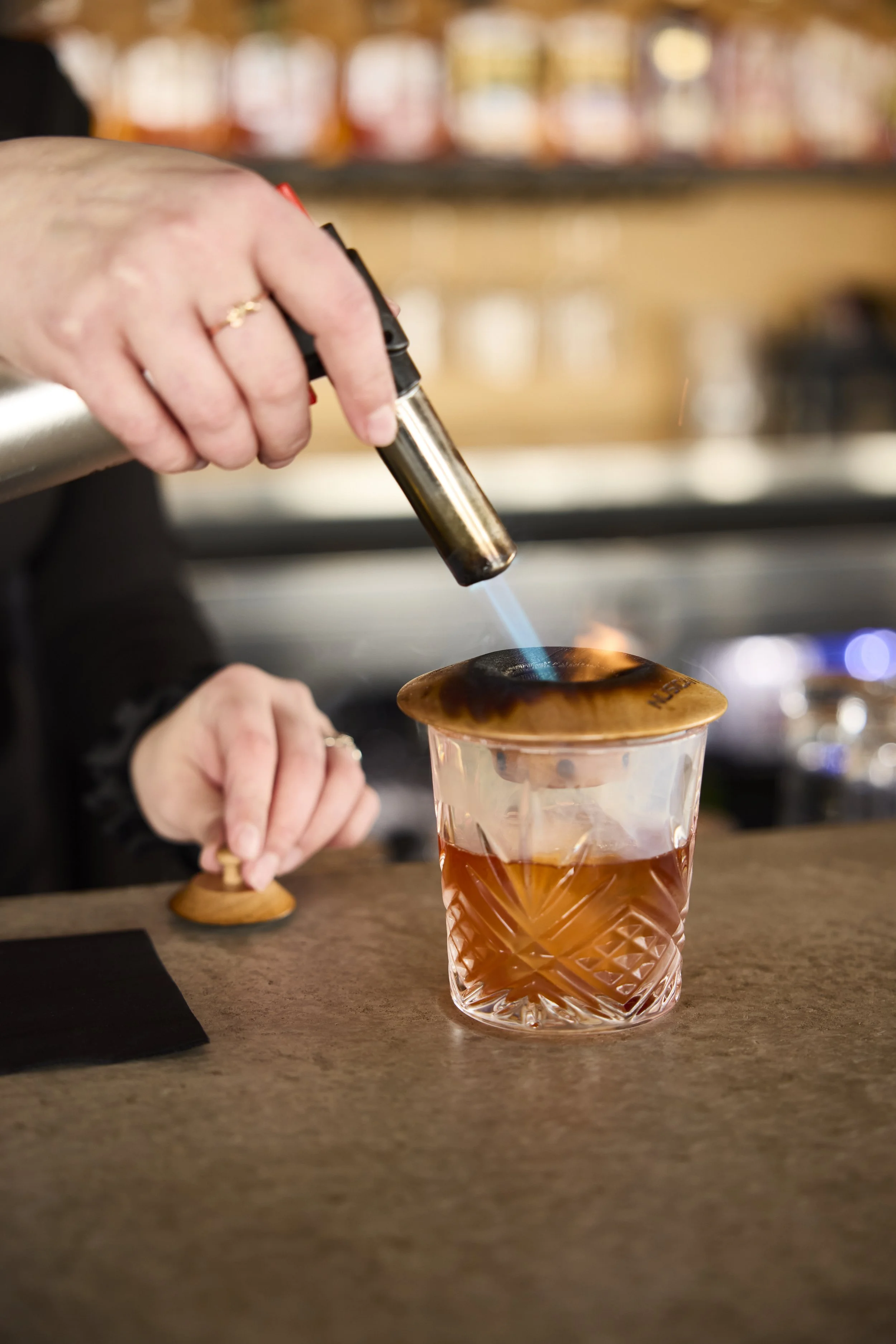 Liberty Tavern beverage featuring a bartender torching an orange peel over a craft cocktail, finishing the drink at the bar with a smoked citrus garnish.