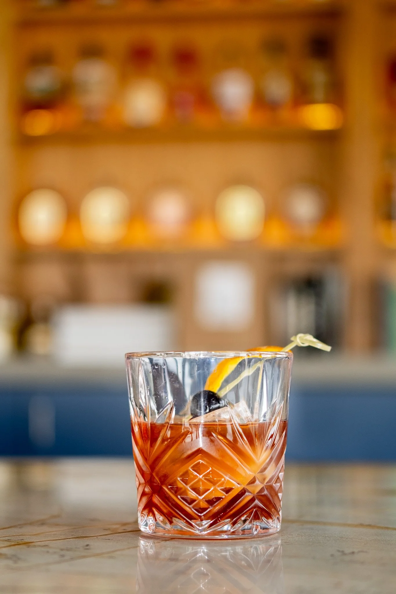 Old fashioned cocktail served at Liberty Tavern Polaris, featuring bourbon, orange peel, and cherry with a softly lit tavern bar in the background.