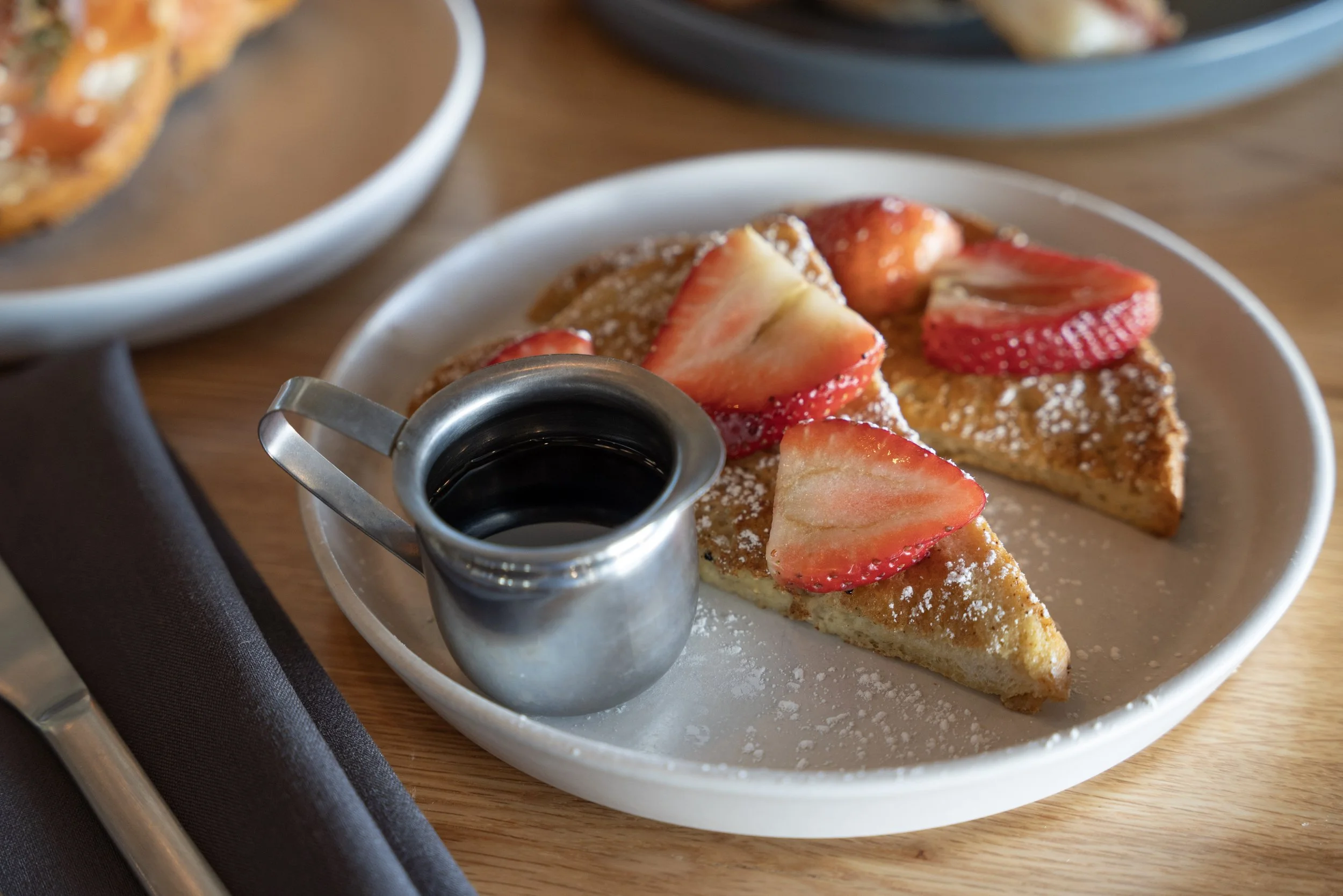 Liberty Tavern brunch featuring thick-cut French toast topped with fresh strawberries and powdered sugar, served with warm maple syrup on a light ceramic plate.