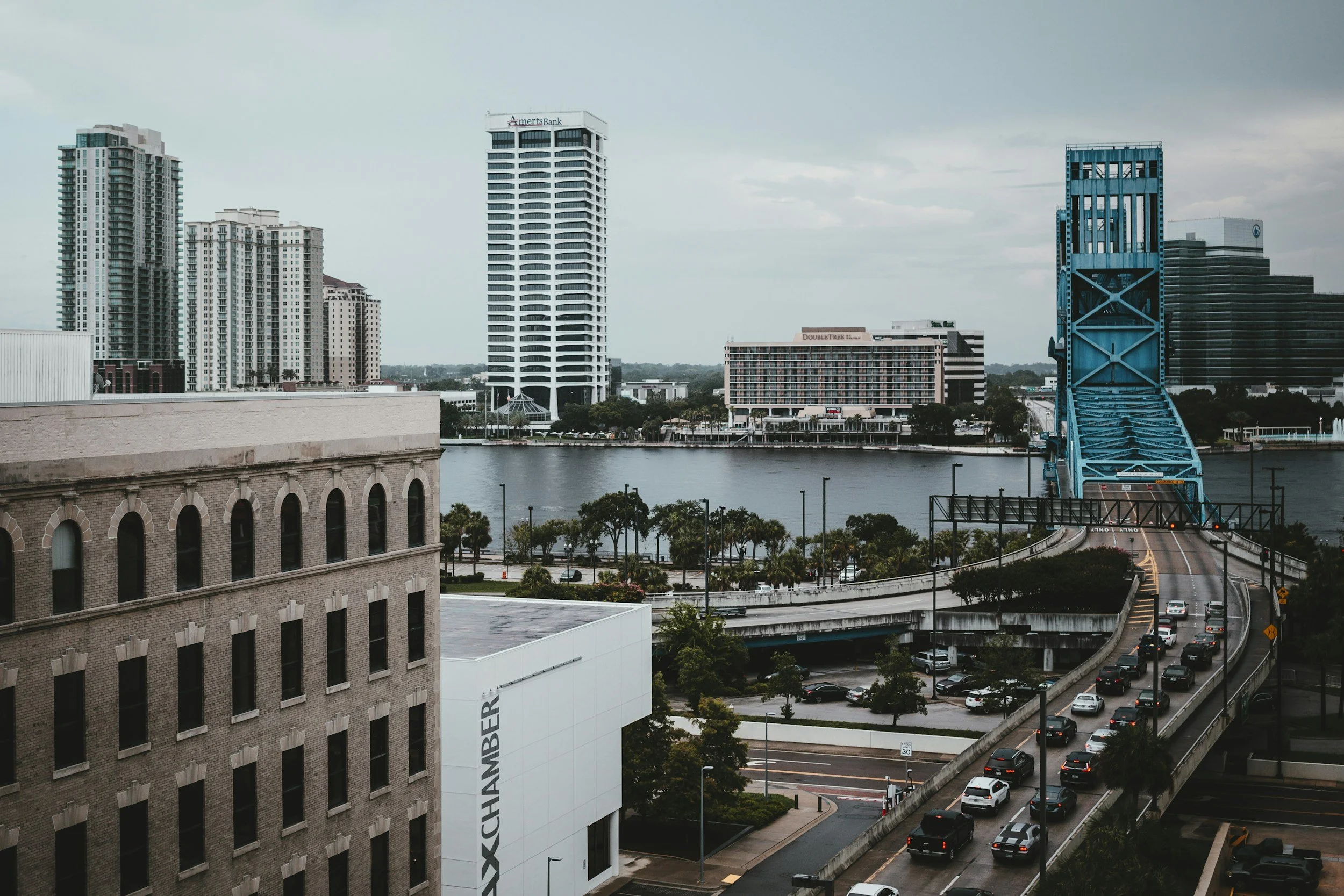 City skyline with tall modern buildings, a bridge over water, and traffic on the roads