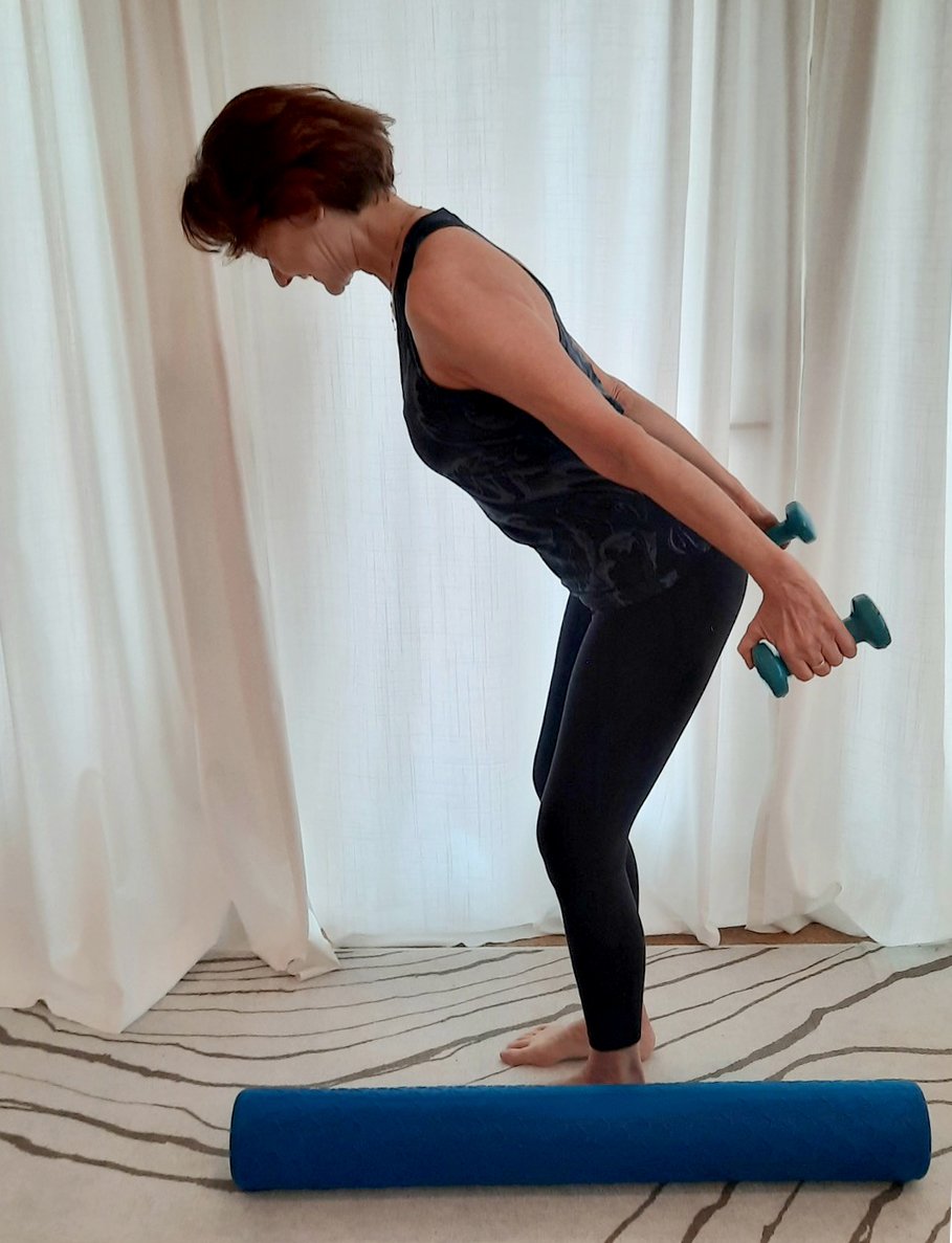  Joy doing a standing exercise with weights in her hands and a melt roller nearby 