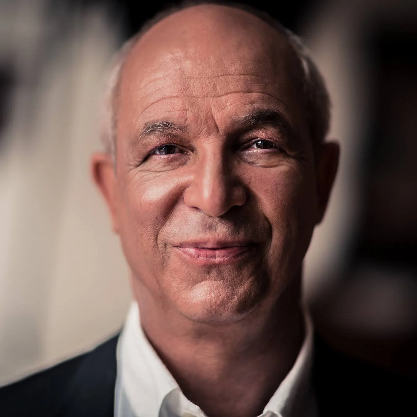 Et nærbillede af en glad, ældre mand med en skaldet hoved, iført en hvid skjorte og mørk blazer.