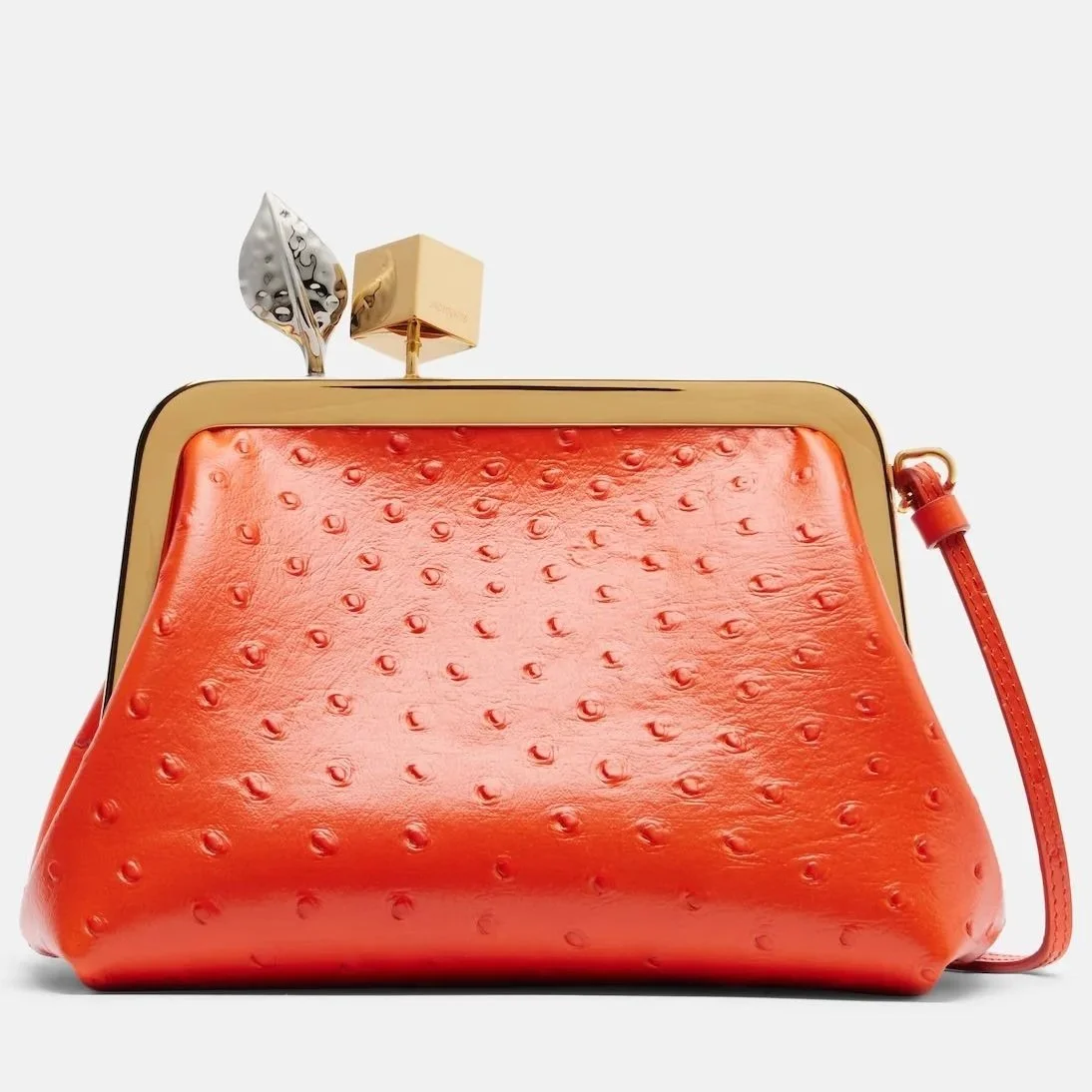 Red handbag with a textured surface and gold accents, decorated with metallic leaves and a small cubic box on top.