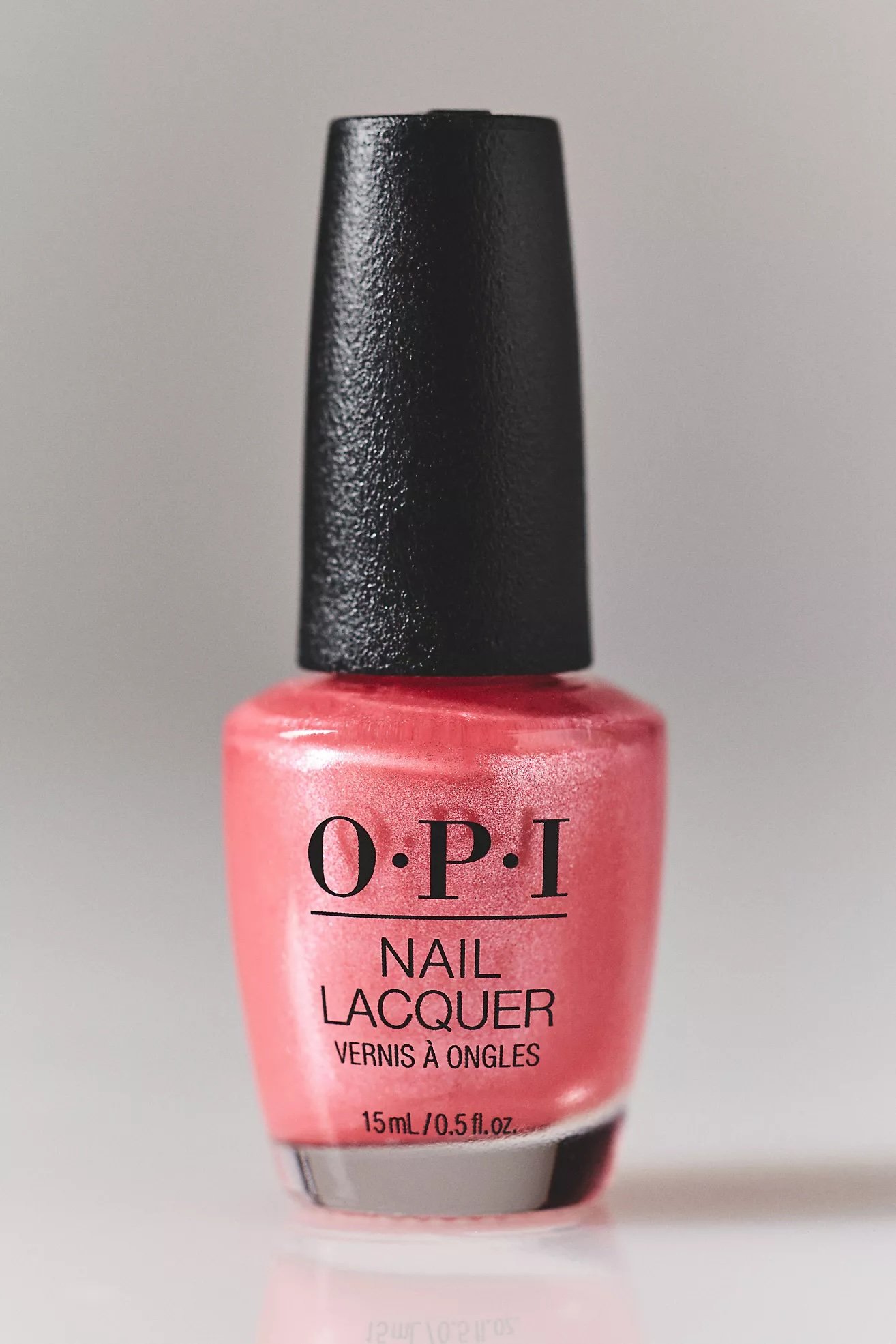 Close-up of a pink OPI nail lacquer bottle with a black cap, positioned against a plain gray background.