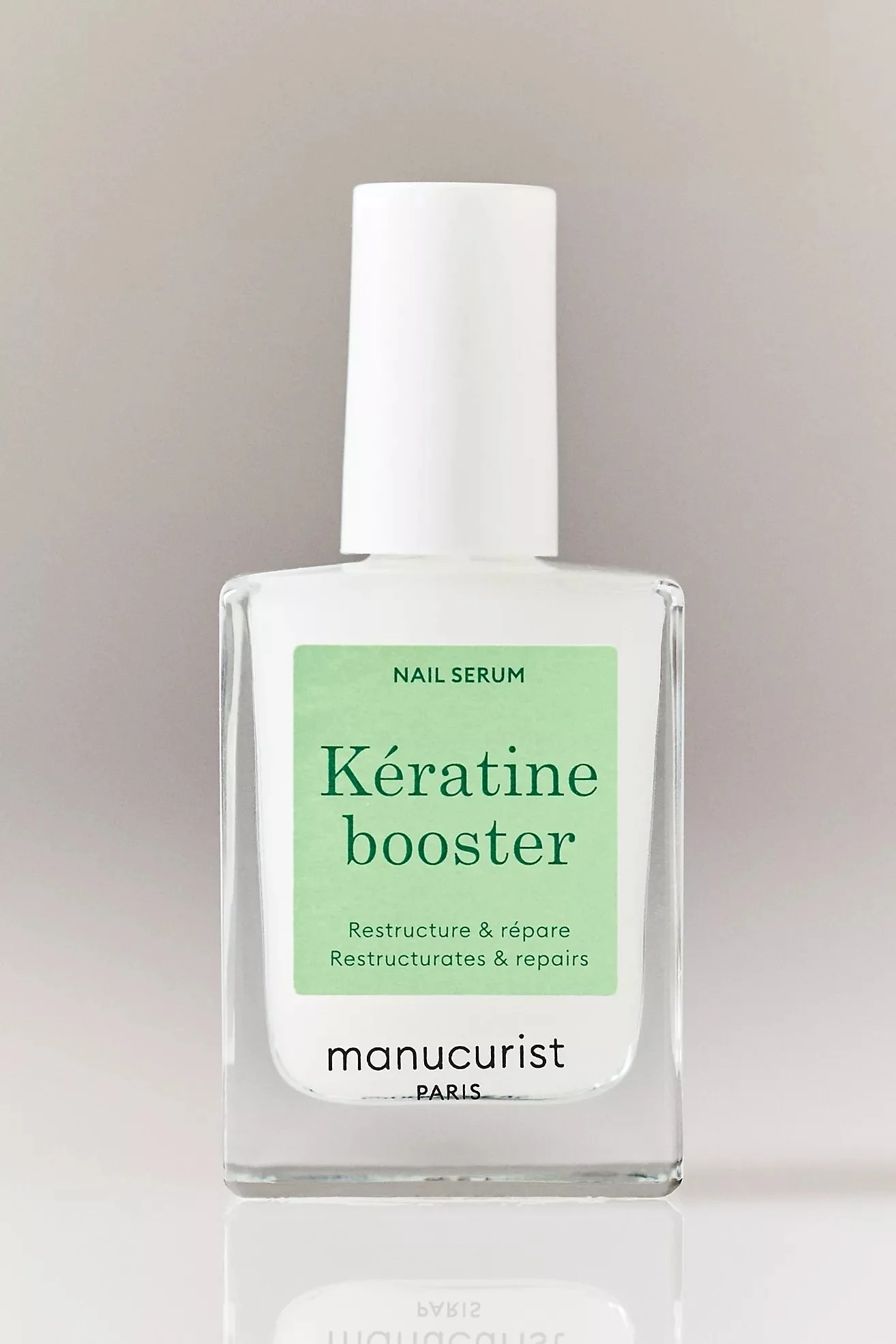 A clear glass bottle of nail serum called 'Kératine booster' by Manucurist Paris, with a white cap and a green label.