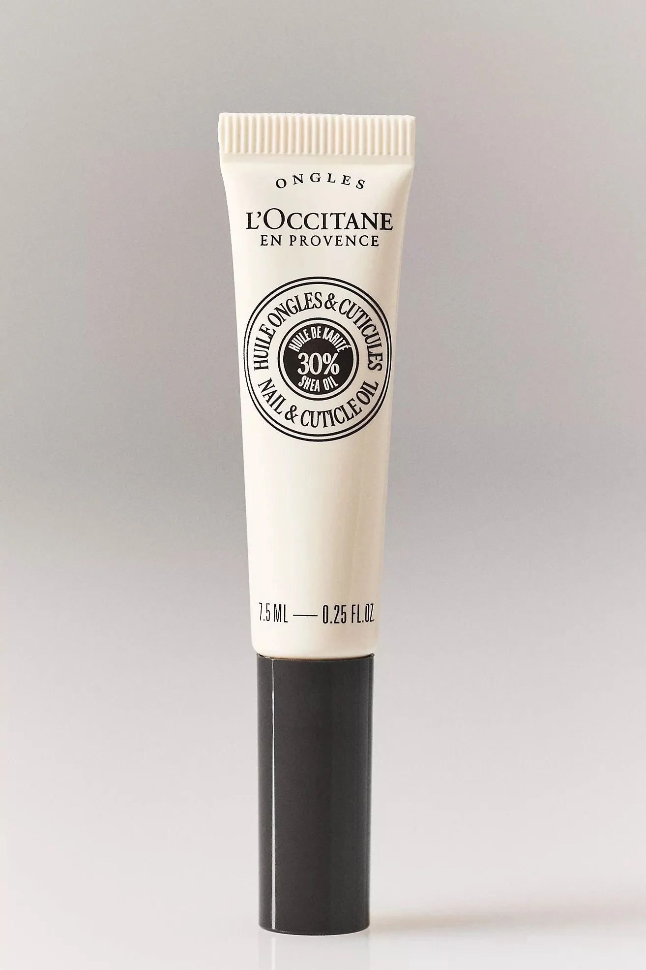 A tube of L'Occitane En Provence nail and cuticle oil with shea butter, standing upright on a black cap against a plain background.