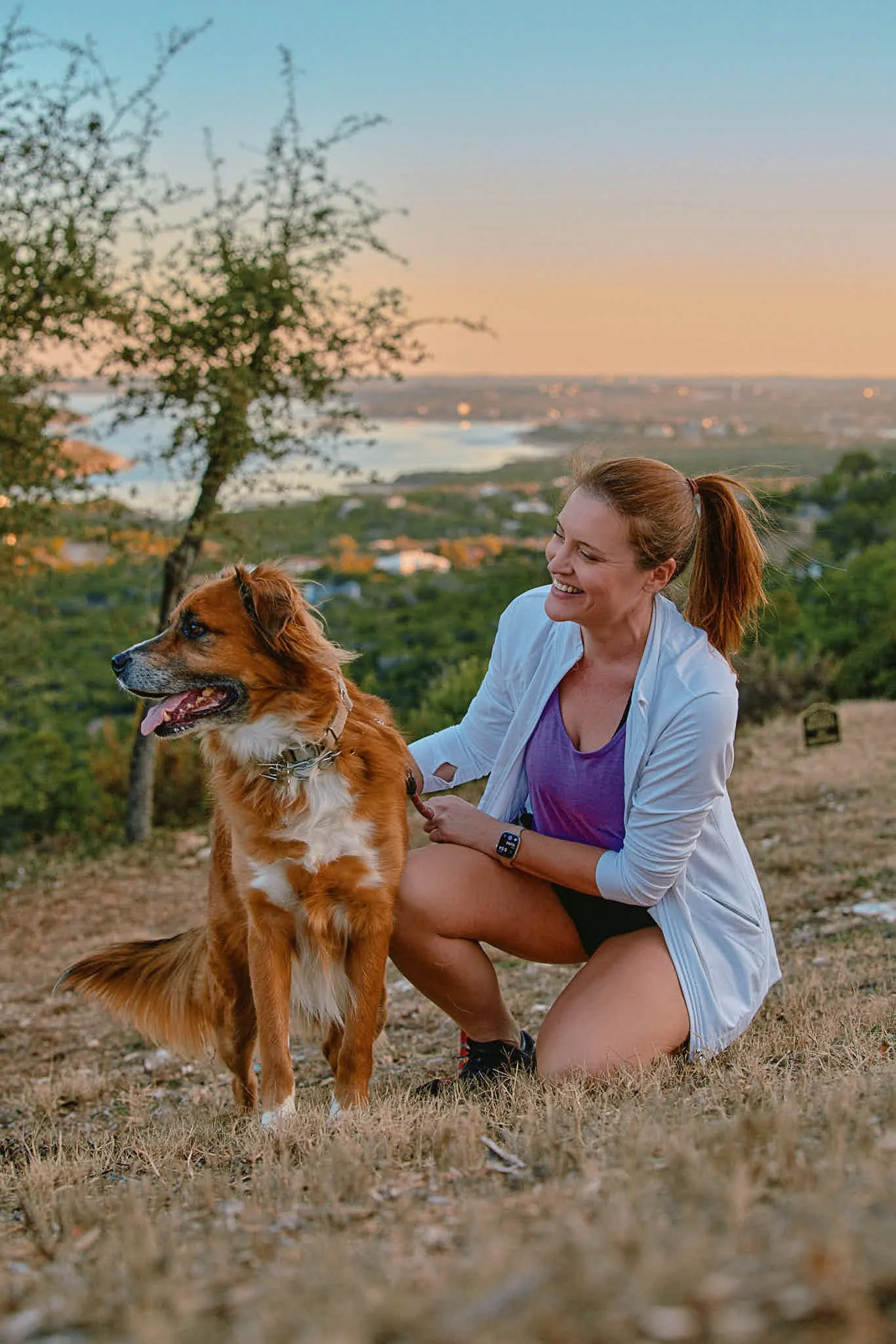 A woman with her dog with Austin City lake in the background at sunset, a casual, fun and cute Austin dating profile photo