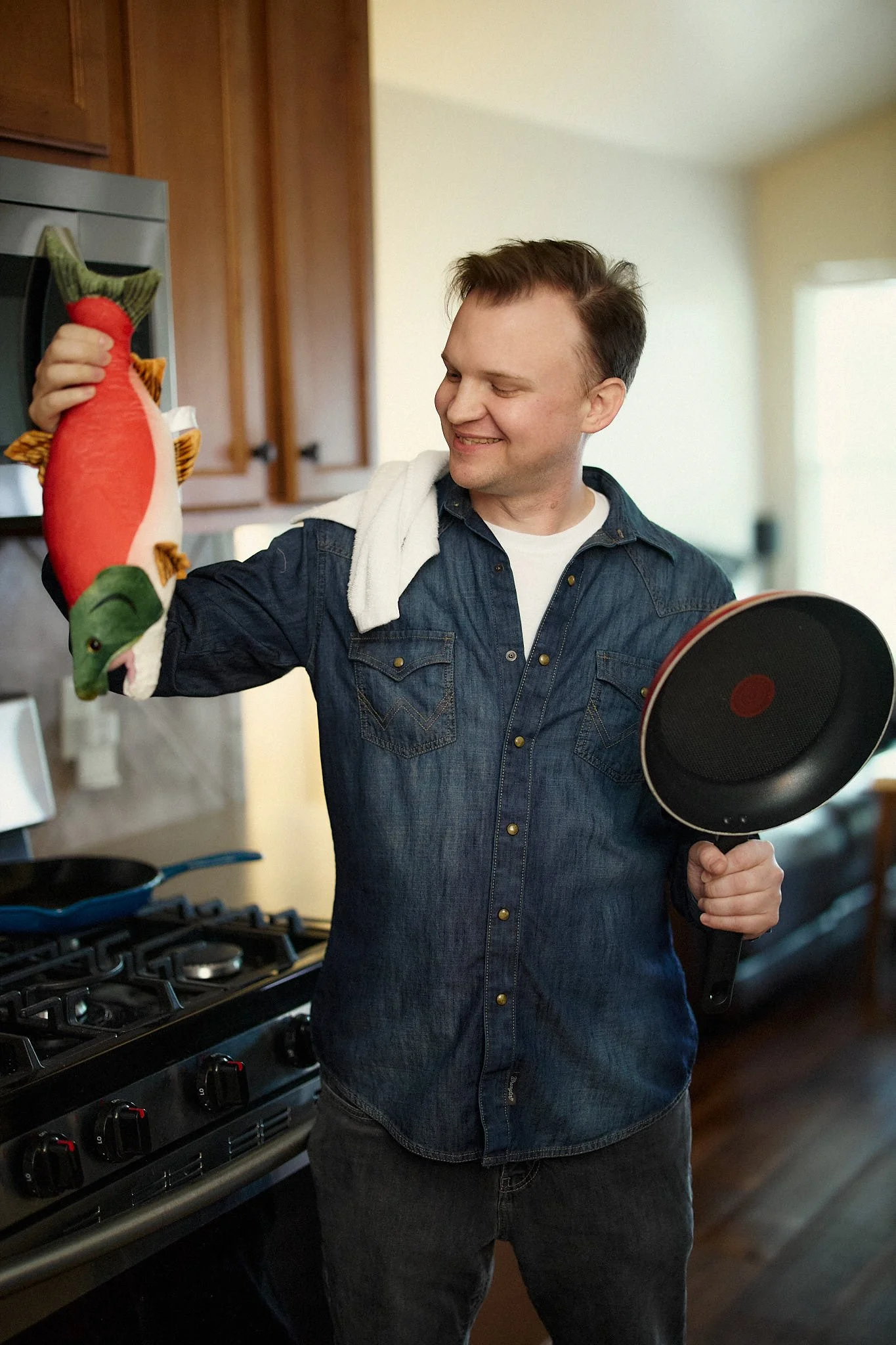 A guy holding a plush toy fish in the kitchen as a joke for his dating profile