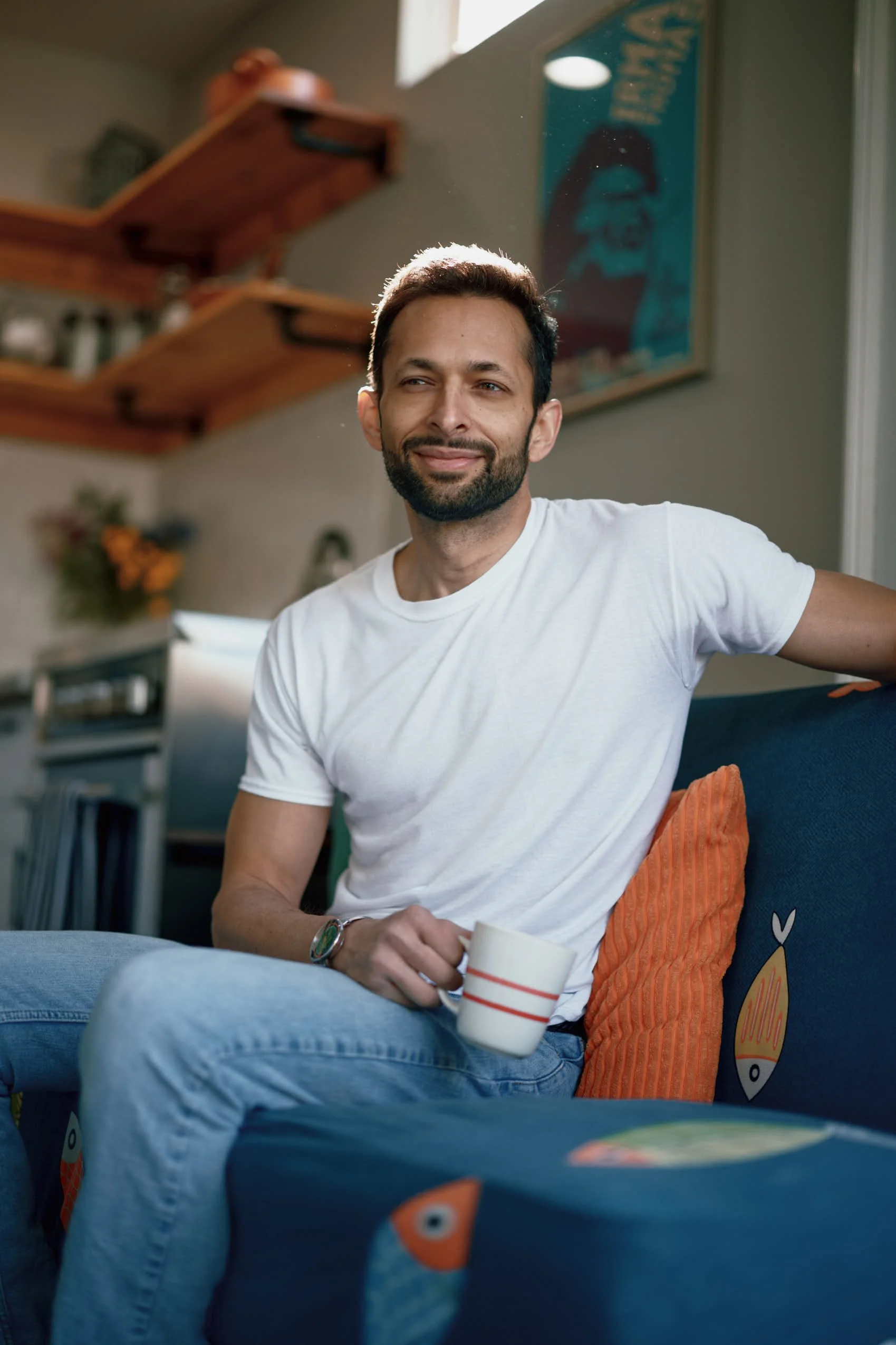 A hero shot of a Indian man sitting in a colorful Airbnb holding a coffee cup